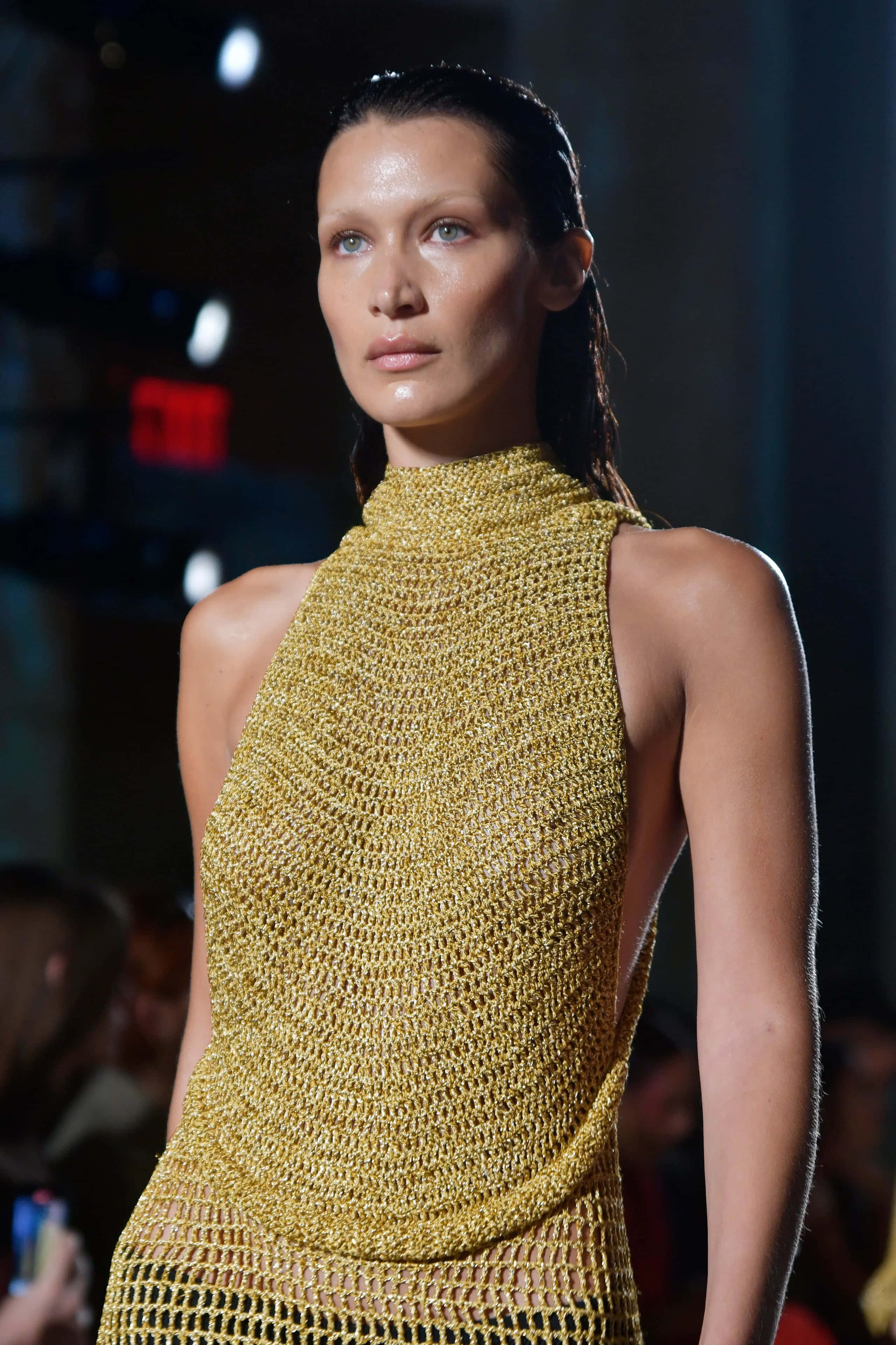 Fashion 桌布 壁紙 — 模特兒自信地穿著閃閃發光的金色鉤針連衣裙，在明亮的時裝展燈光下行走。
