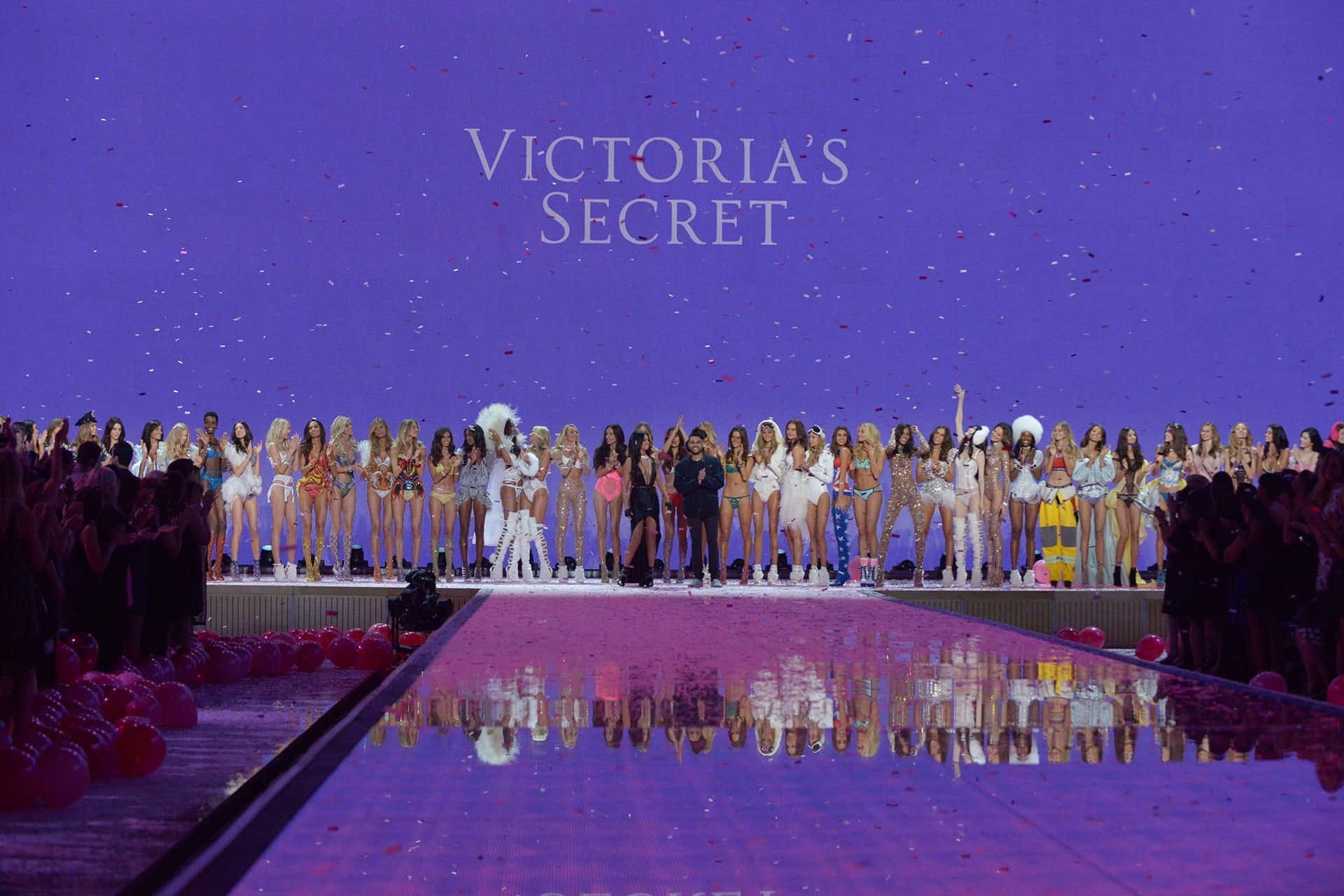Victoria's Secret 桌布 壁紙 — 模特兒身穿閃亮內衣，在紫色天橋上勝利地站立，'Victoria's Secret'標牌下五彩紙屑如雨般灑落。