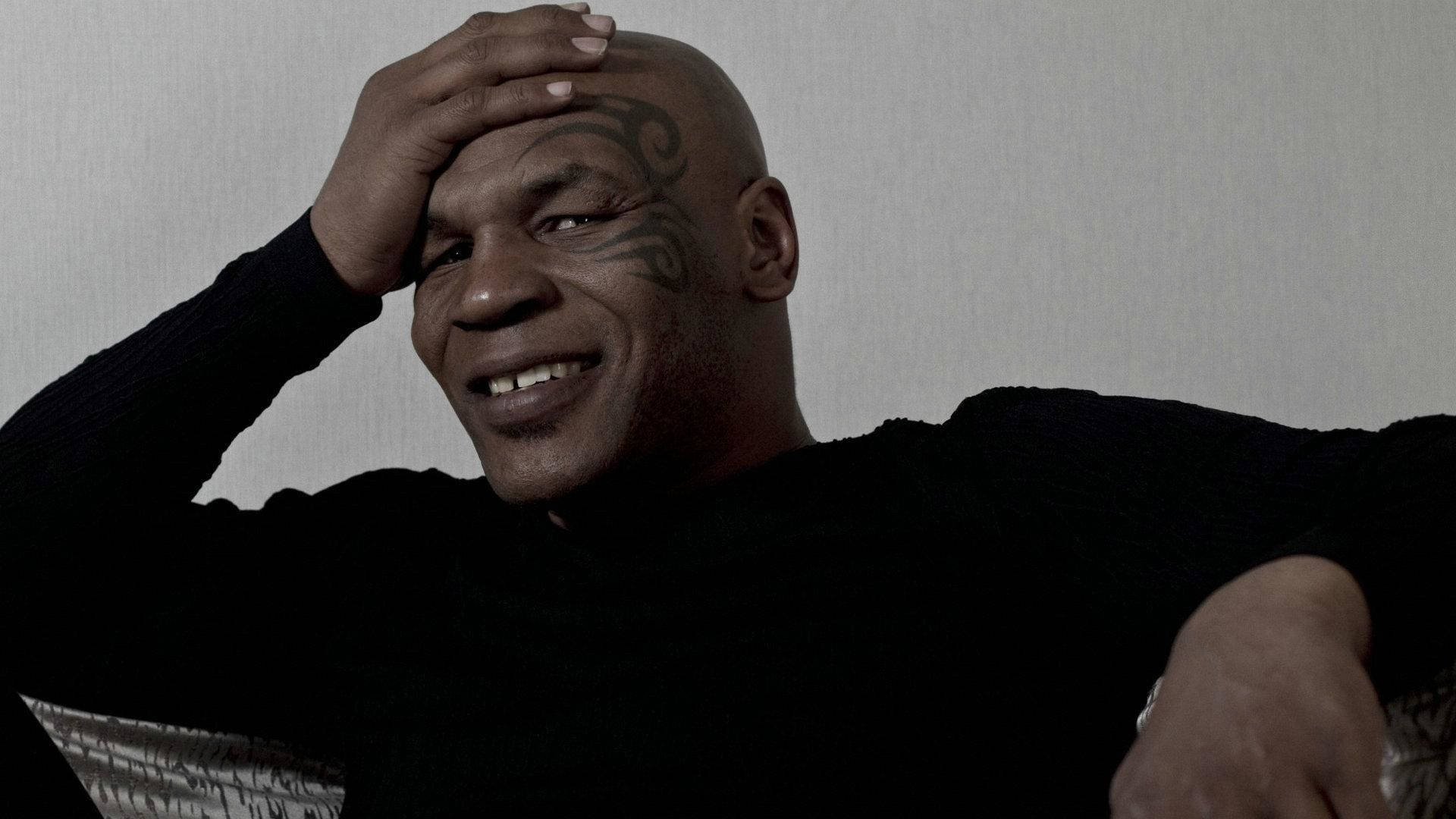 模特兒邁克·泰森 壁紙 — Mike Tyson 喺昏暗燈光下對住素色牆壁，將手放喺額頭上溫暖咁微笑。