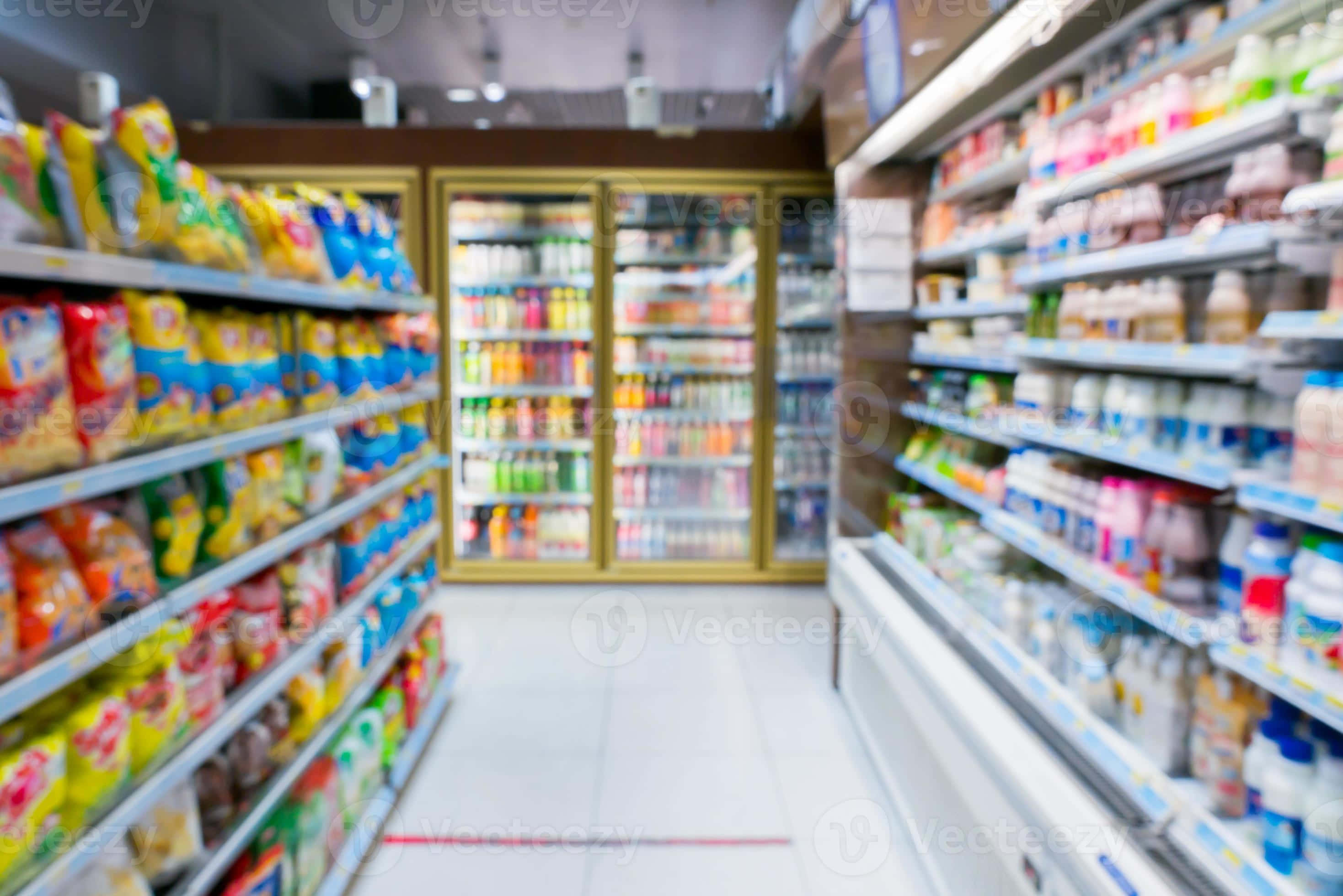 Grocery Store 桌布 壁紙 — 模糊的雜貨店通道，色彩繽紛的零食貨架和冷藏櫃在明亮的燈光下閃閃發光。