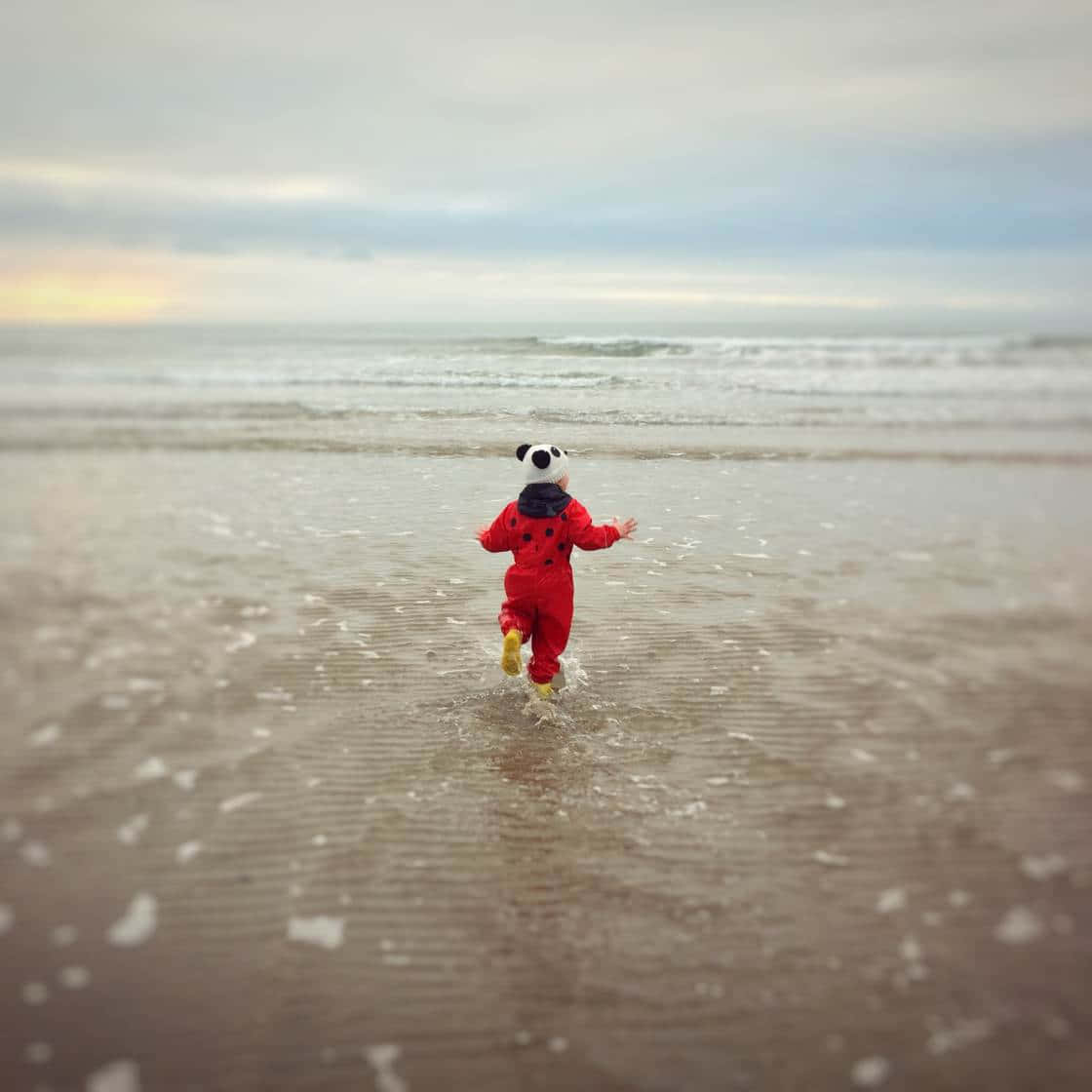 一個穿著紅色瓢蟲服裝的孩子在日落時跑進海浪中。