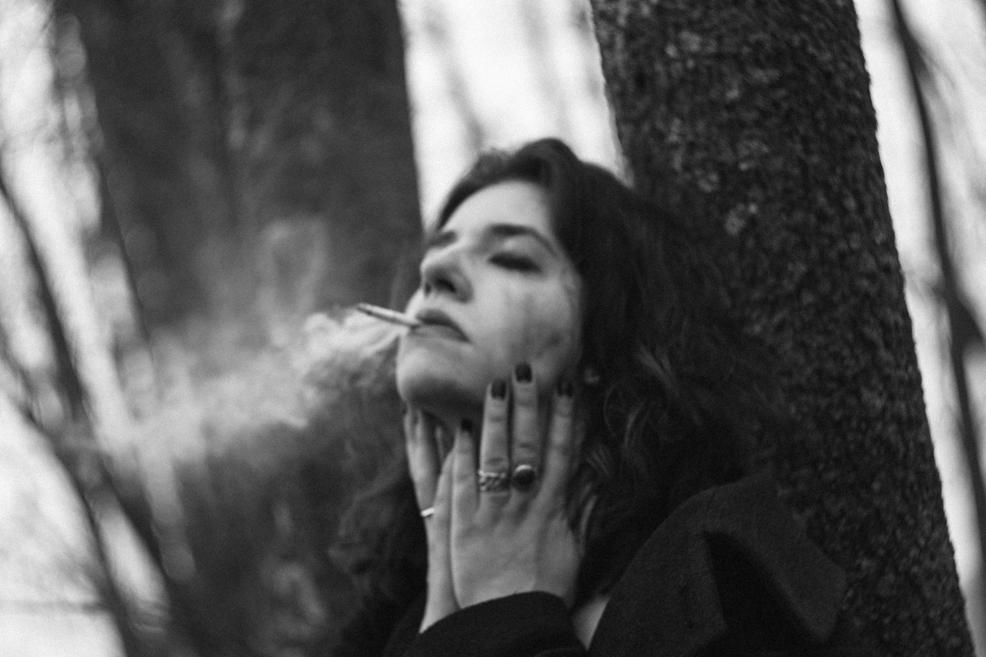 黑白肖像中靠著樹抽煙的女士
