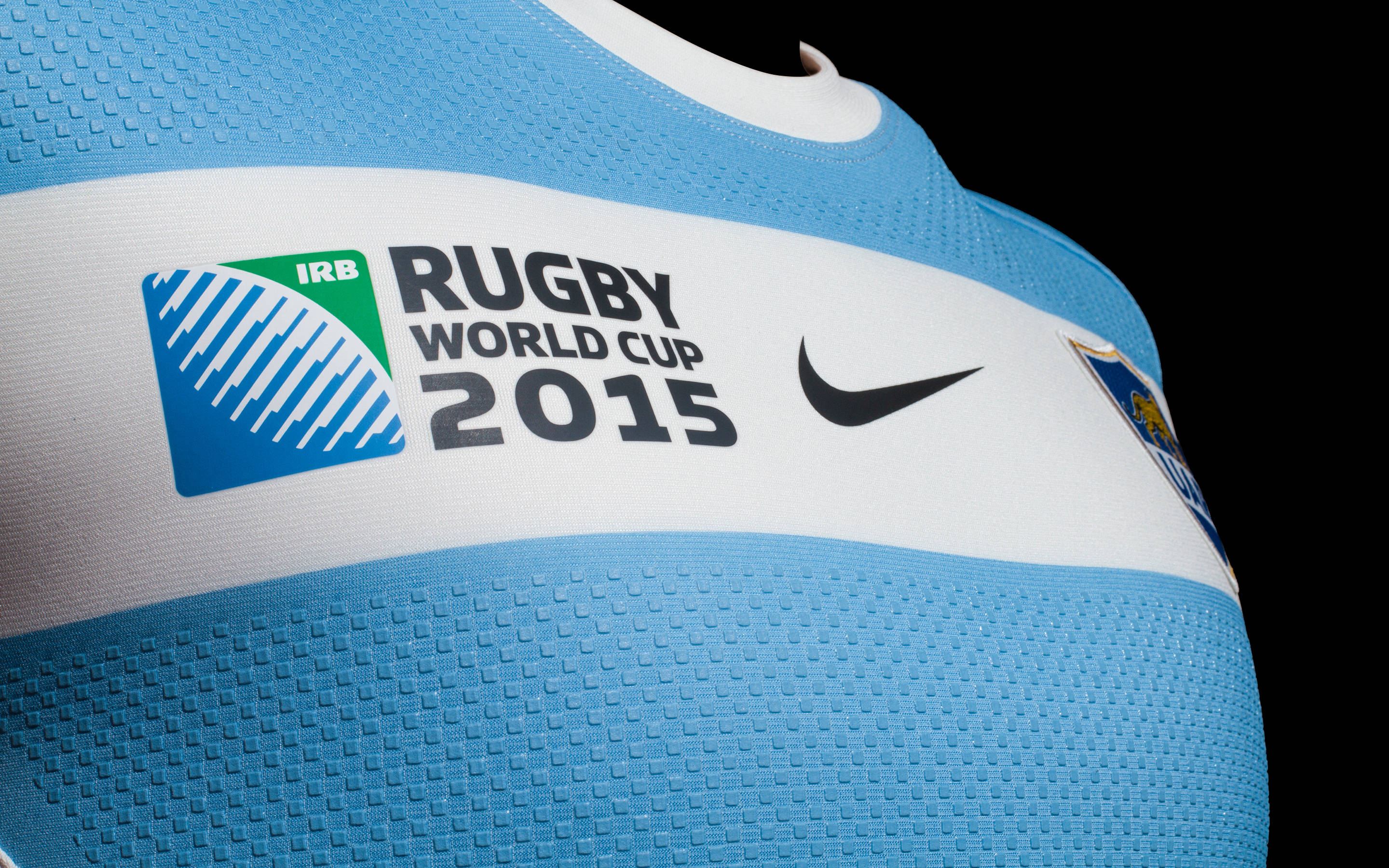橄欖球世界盃耐克 iPhone 壁紙 — 特寫一件淺藍色欖球球衣，上面有IRB Rugby World Cup 2015標誌和Nike swoosh，背景為黑色。