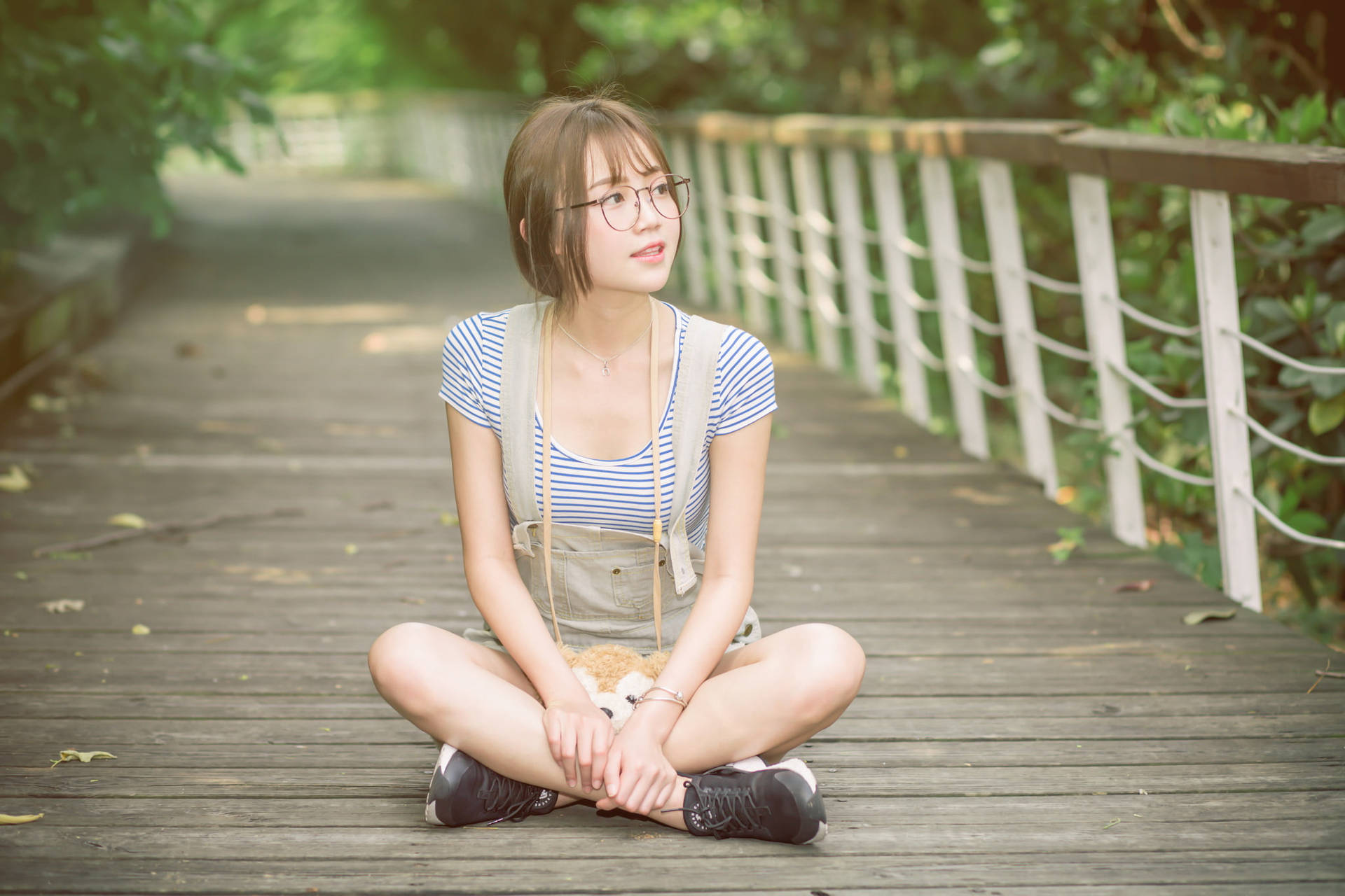 戴眼鏡的年輕女性盤腿坐在公園的木製步道上。
