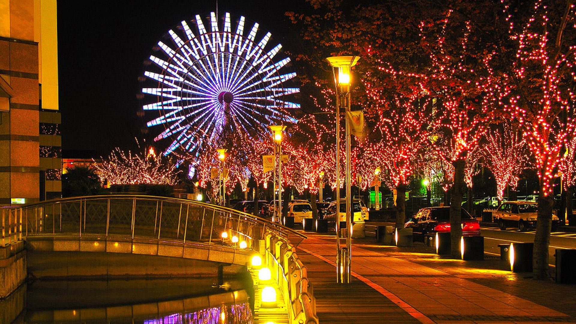 橙城摩天輪夜色浪漫 壁紙 — 一個充滿活力的夜景，特色是發光的摩天輪和沿著行人天橋被紅燈包裹的樹木。