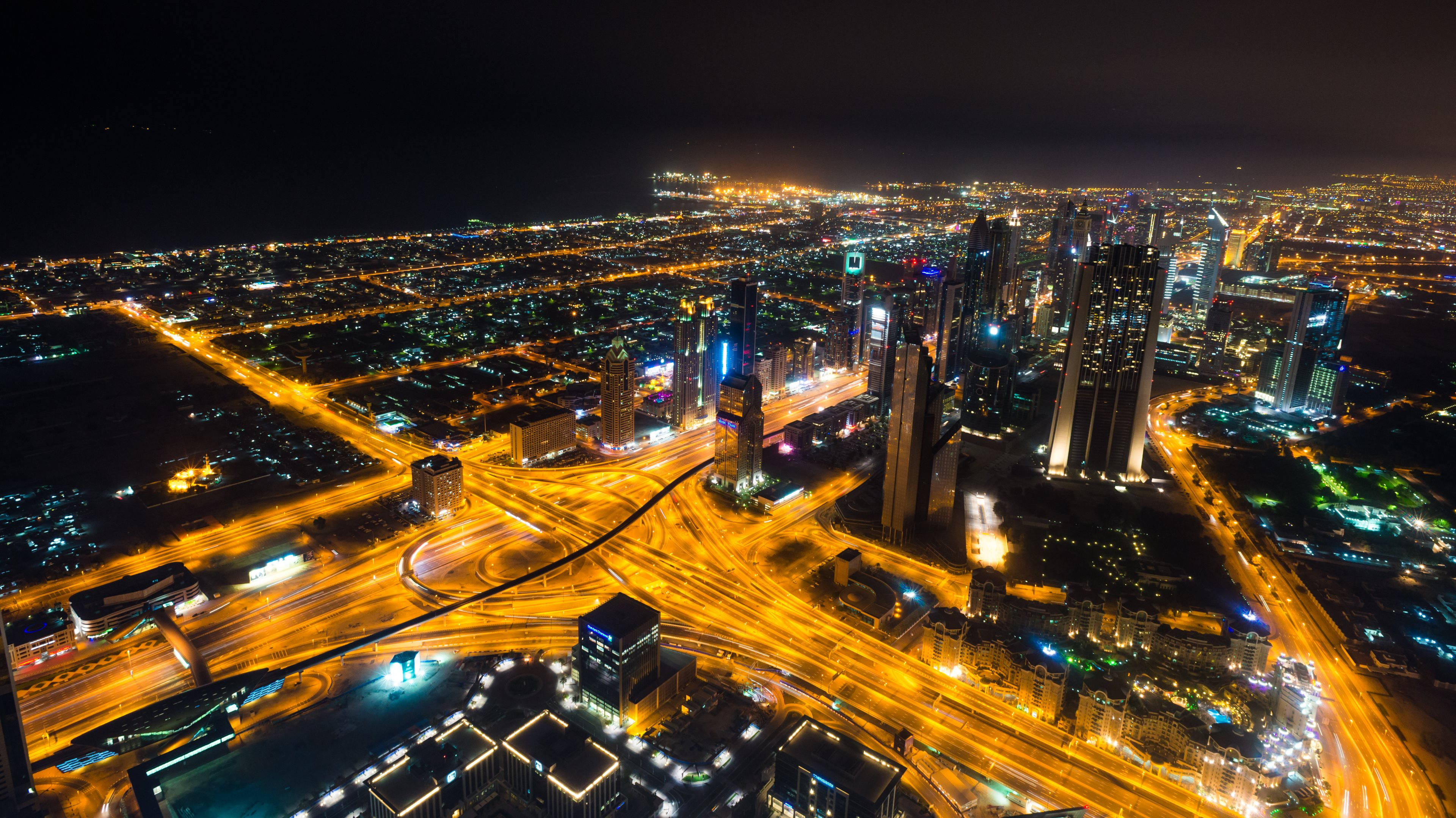 橙城道路夜景延時攝影 壁紙 — 廣闊城市景觀的空中夜景，發光的摩天大樓和照明的高速公路穿過密集的城市擴張。