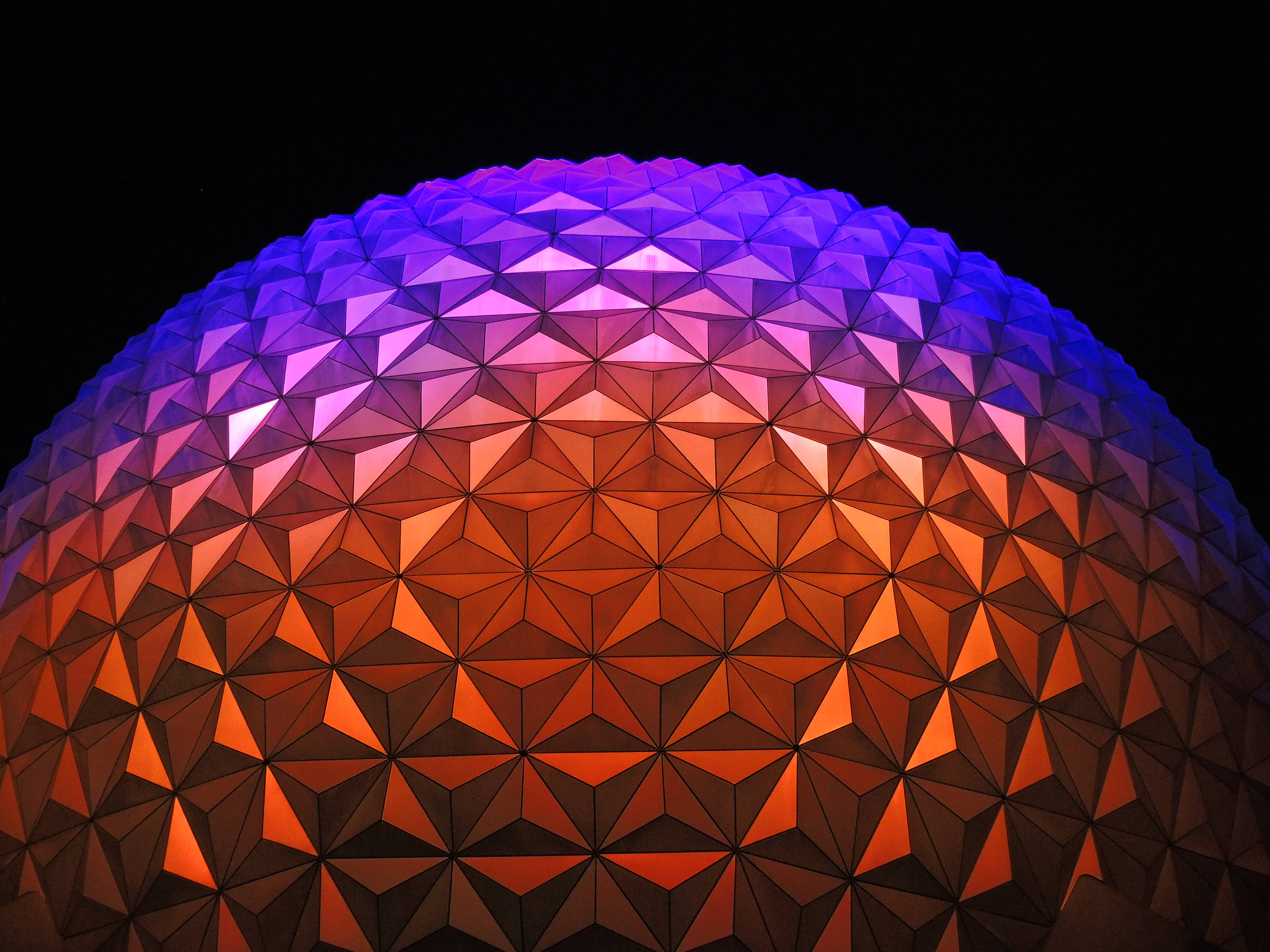 橙紫漸層 Epcot 球體 壁紙 — 一個測地線穹頂的特寫，在黑色夜空下發出鮮豔的紫色和橙色光芒。