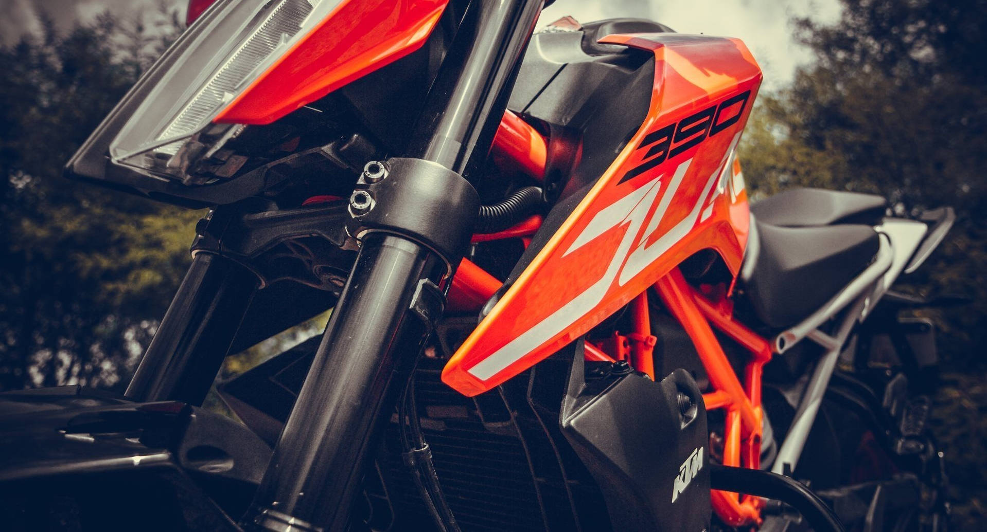 一輛鮮橙色KTM 390越野電單車帶有黑色點綴，停放在森林中。