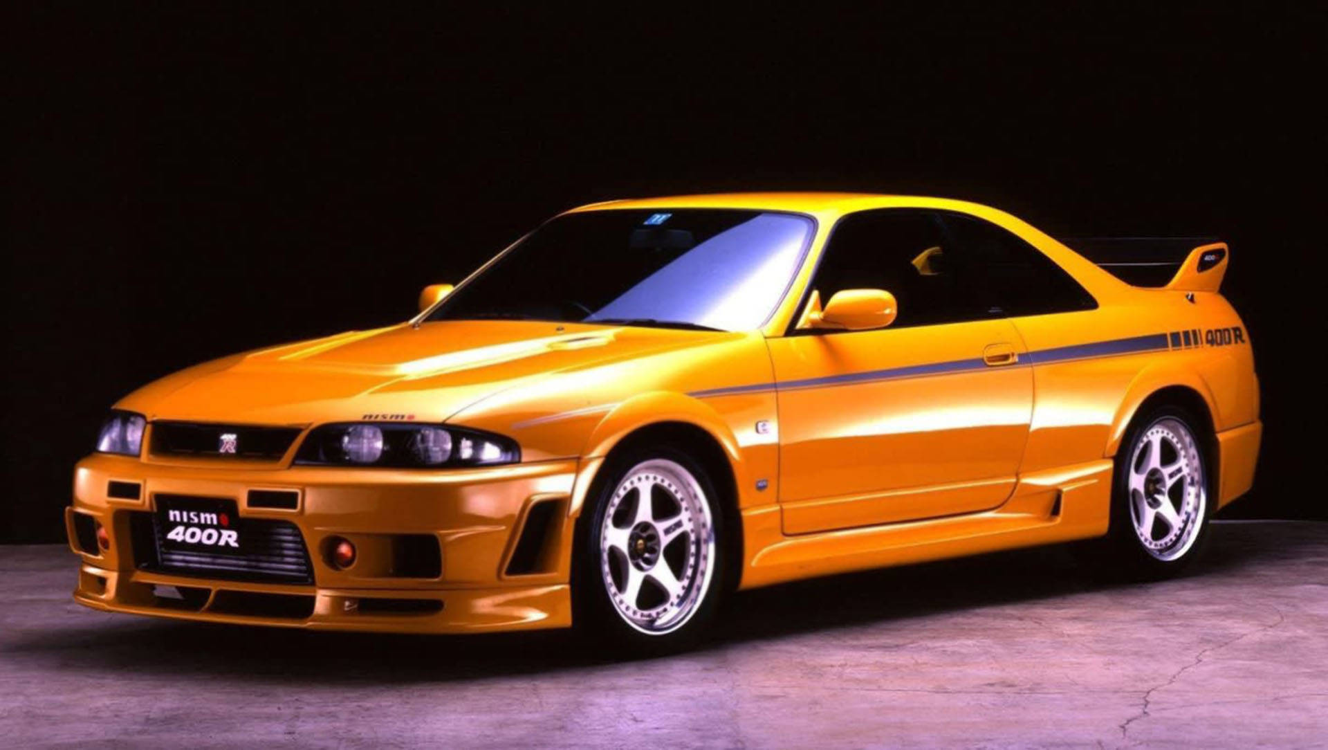 攝影棚燈光下的橙色日產Skyline R34 Nismo 400R跑車。