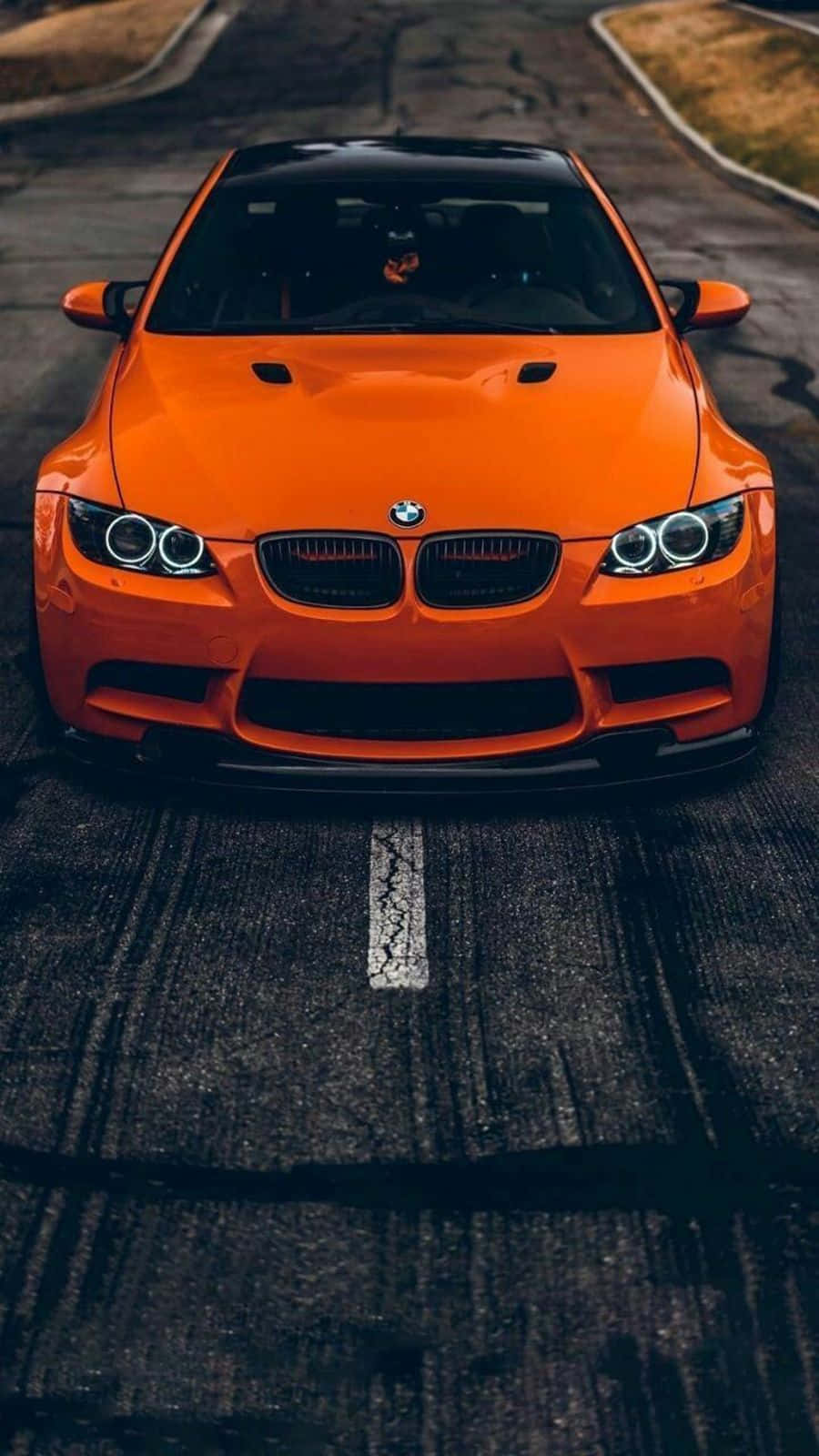 橙色BMW跑車在深色道路上，帶有輪胎痕和一條裂紋白線。