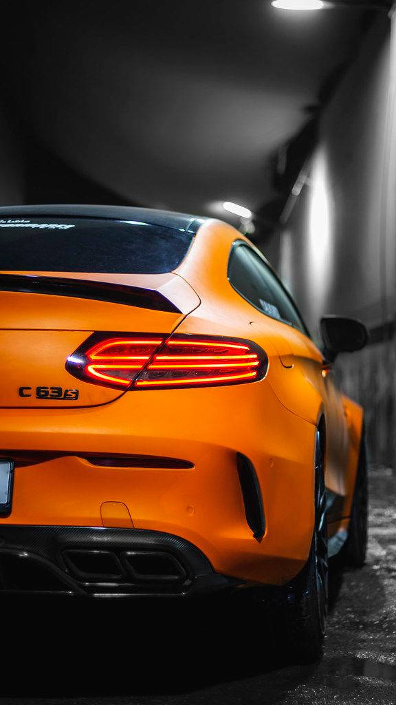 橙色AMG車尾特寫 壁紙 — 鮮橙色 Mercedes-AMG C63 S 雙門跑車，帶有發光的紅色尾燈，停在光線昏暗的隧道中。