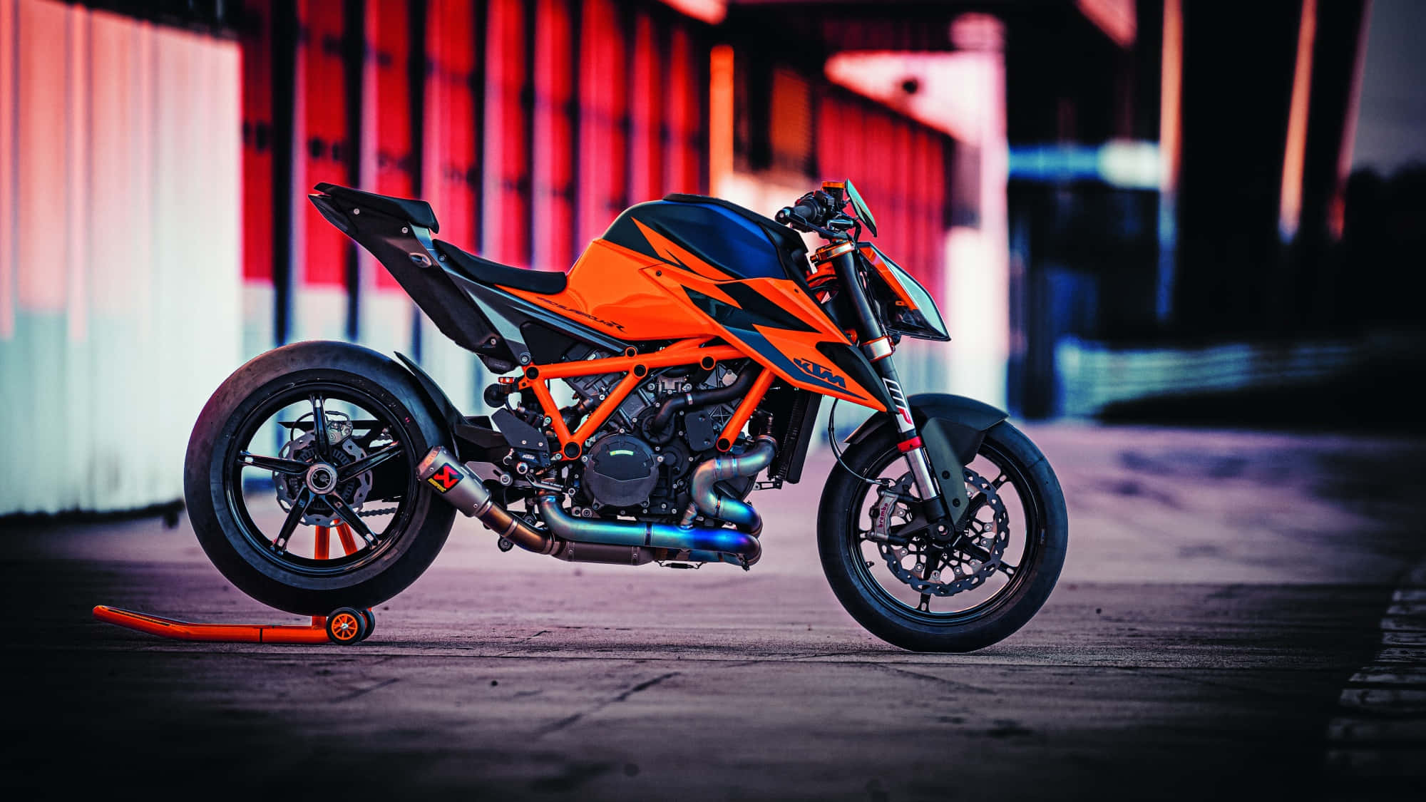 橙色KTM 1290 Super Duke GT停泊於港口照片 壁紙 — 一輛鮮豔的橙色KTM電單車用側腳架停放在一條光線昏暗的城市小巷中，帶有紅色和藍色的霓虹燈反射。