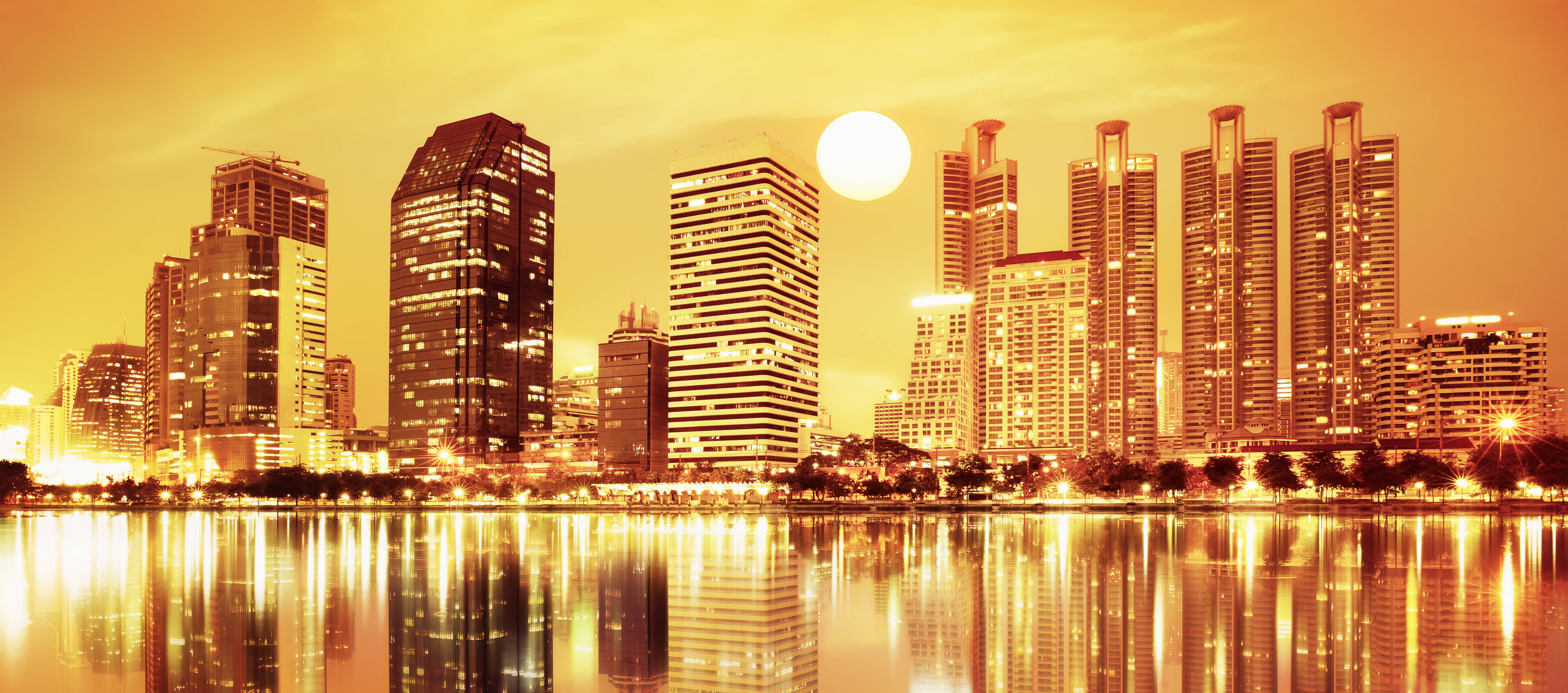 橙色城市摩天大樓 壁紙 — 金色夕陽以溫暖光線沐浴現代摩天大樓，它們的倒影在下方平靜水面上閃爍。