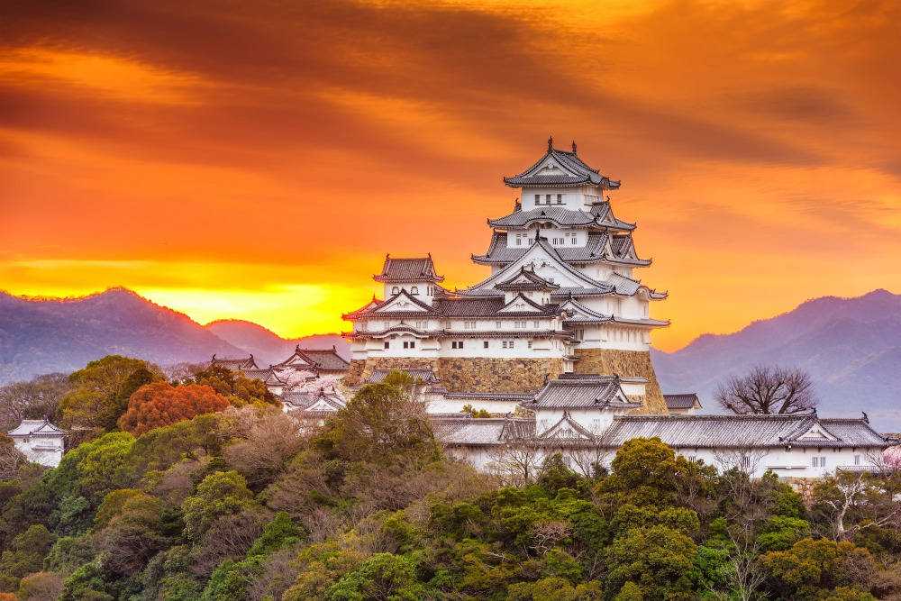 在充滿活力的橙色日落中，山丘上的白色日本城堡，背景有山脈。