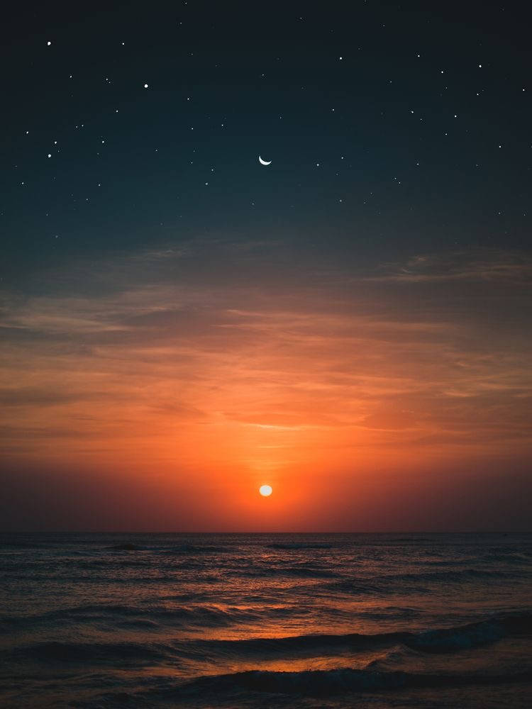 橙色太陽與彎月 壁紙 — 暮色中寧靜的海洋，發光的太陽沉入地平線以下，新月和星星出現在漸暗的天空中。