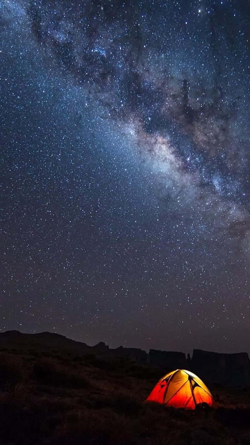 一個發光的橙色帳篷在星空夜空下，銀河可見。
