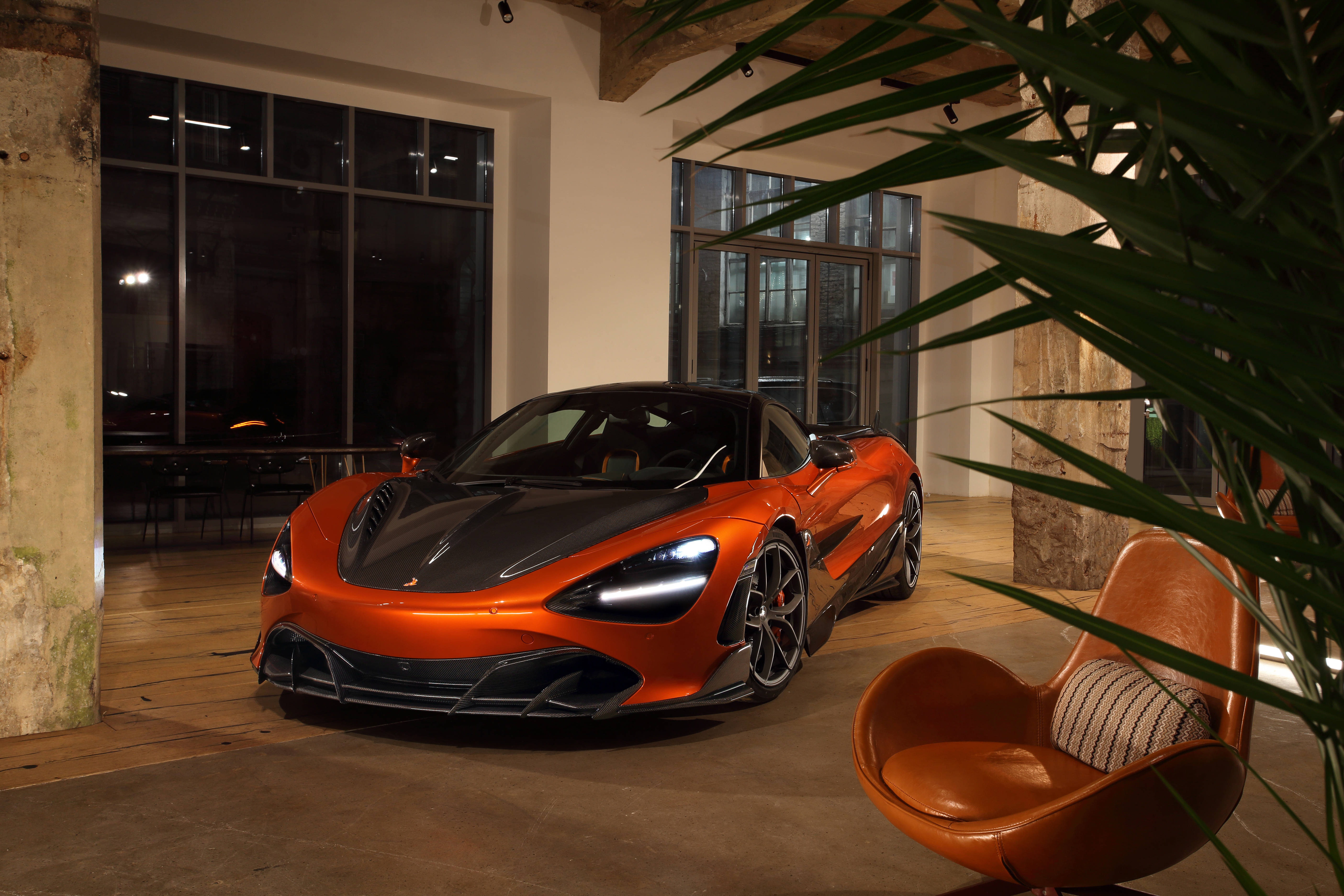 橙色麥拉倫720s停泊於豪華別墅 壁紙 — 一輛充滿活力的橙色McLaren跑車在溫暖的室內燈光下，在皮革椅和熱帶植物旁邊閃閃發光。