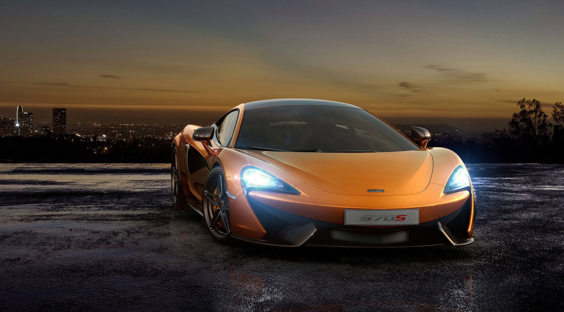 橙色McLaren 570S跑車停在日落時分的濕屋頂上，背景是城市燈光。