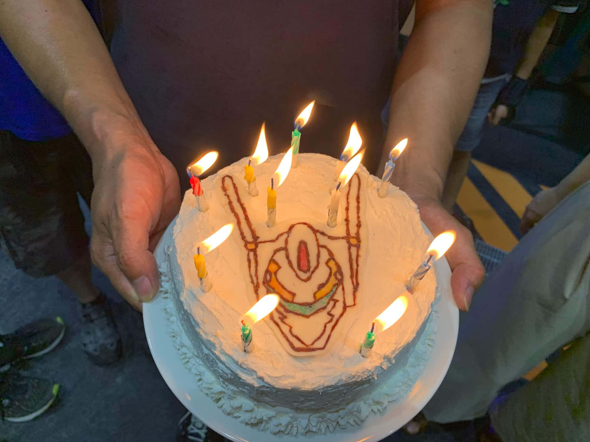 雙手捧著一個生日蛋糕，上面有燃點著的蠟燭，形狀像機械人臉。