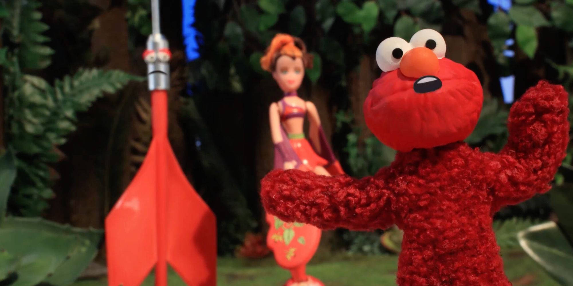 機器雞模仿《艾摩》 壁紙 — Elmo 喺叢林場景中企喺紅色火箭前面，手拎住一個公仔。
