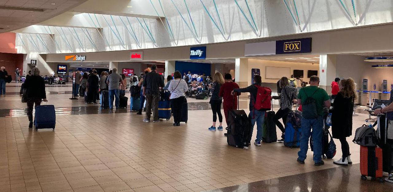 一群旅客帶著行李箱在機場客運大樓等候。