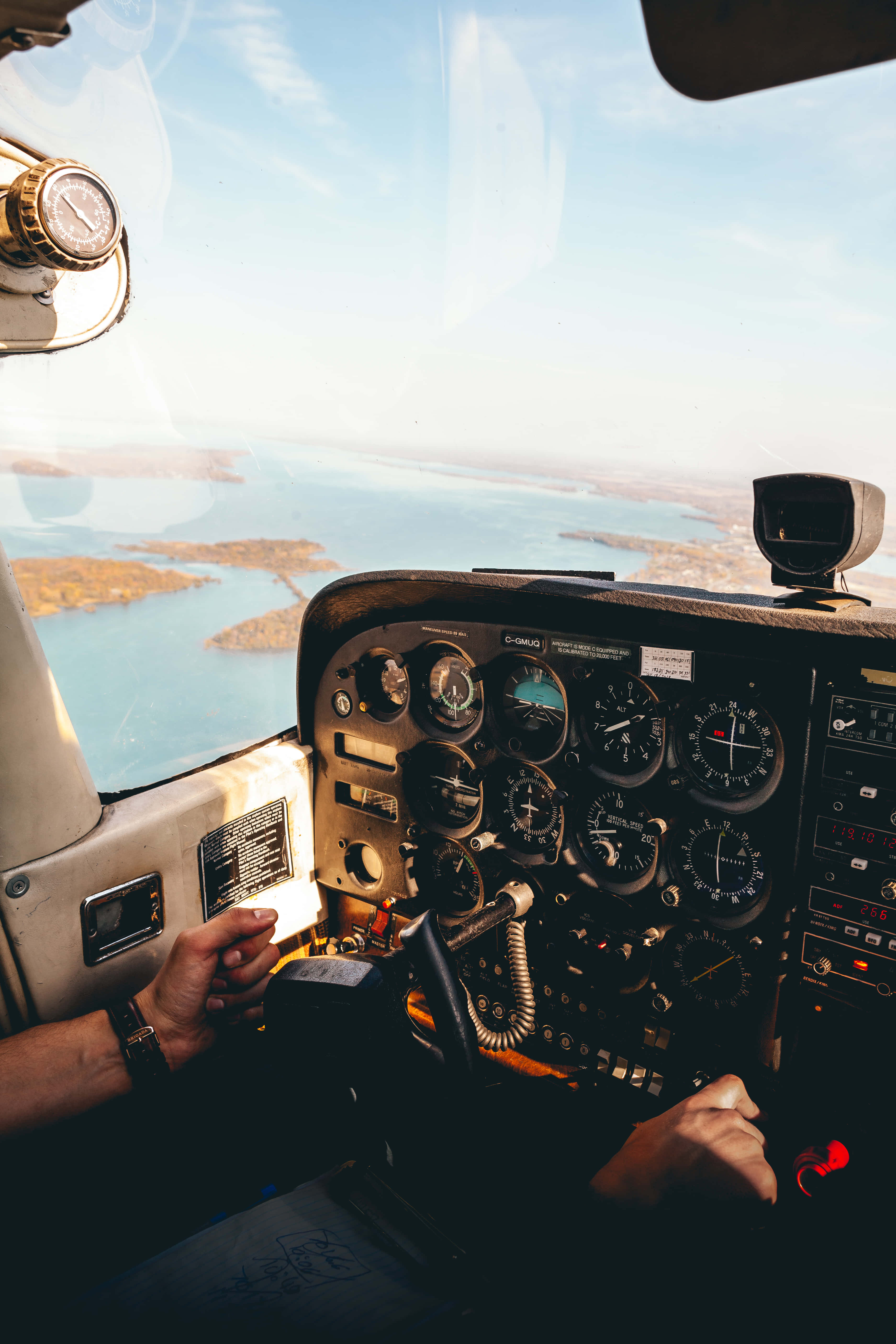 Aviation 桌布 壁紙 — 機師雙手緊握小型飛機駕駛艙內的控制裝置，俯瞰陽光普照的海岸景觀，碧綠海水與零星島嶼盡收眼底。
