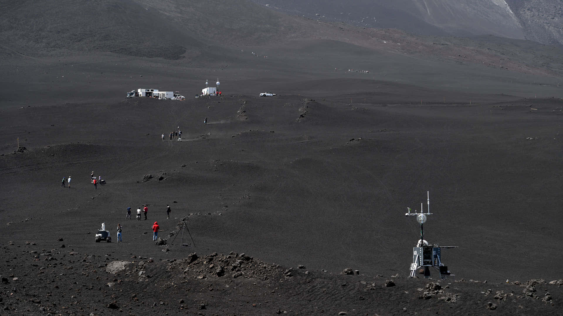 機械人探勘埃特納火山月球地形 壁紙 — 科學家探索廣闊的黑色火山地貌，研究車輛和設備散落在崎嶇的地形上。