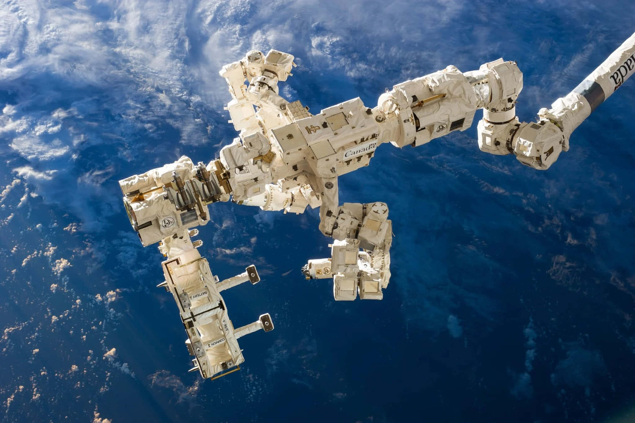 Space Station 桌布 壁紙 — 機械臂從國際太空站伸出，背景是地球的藍色海洋和白色雲層。