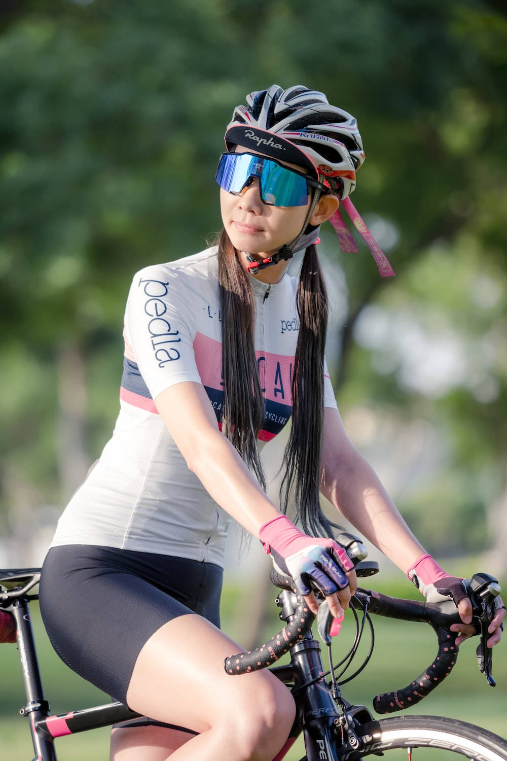 一位穿著單車裝備的女性，在陽光明媚、綠樹成蔭的公園裡騎著公路單車。