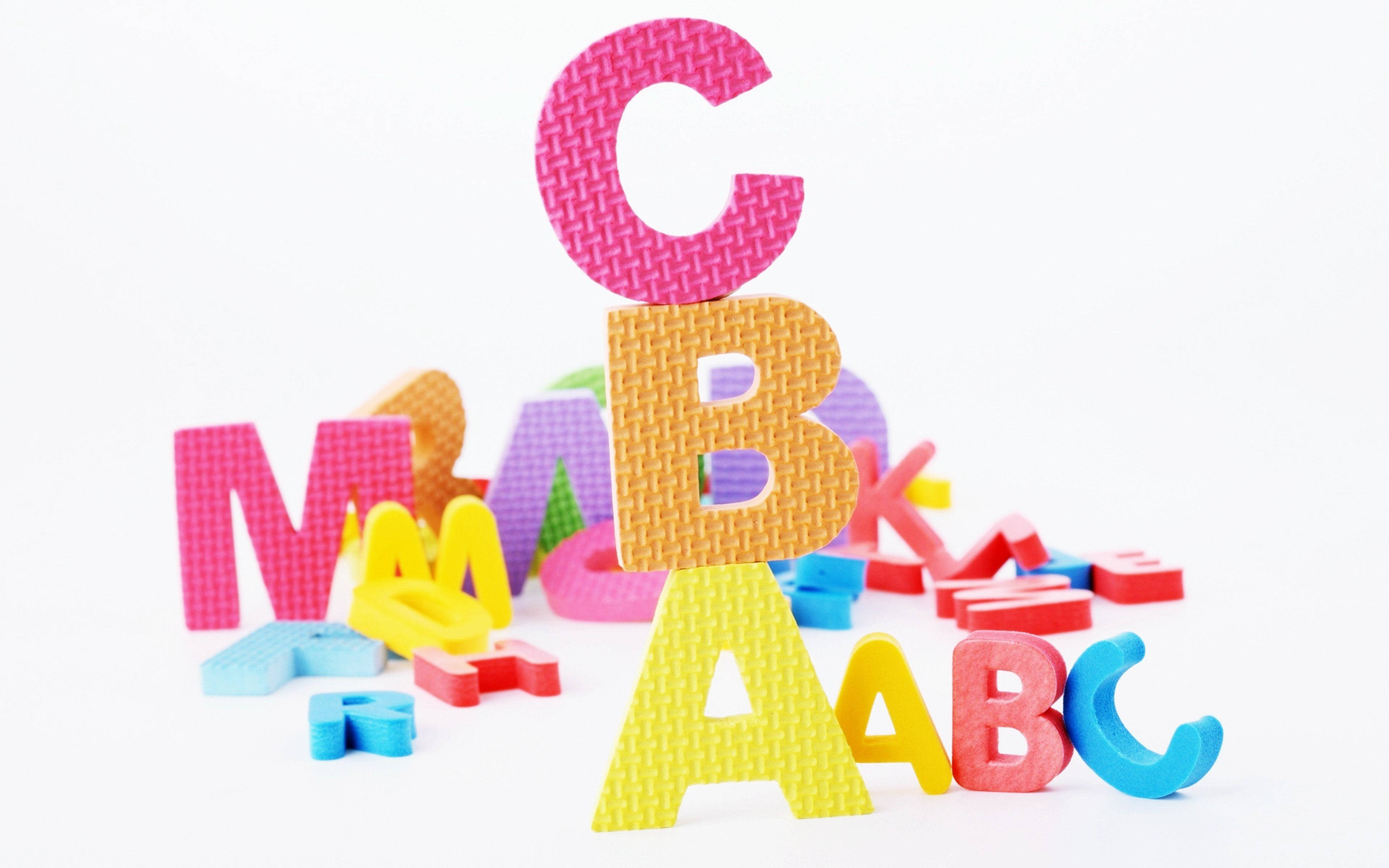 橡膠質感字母ABC 壁紙 — 色彩繽紛的泡沫字母積木堆疊成一個有趣的塔，背景是乾淨的白色。