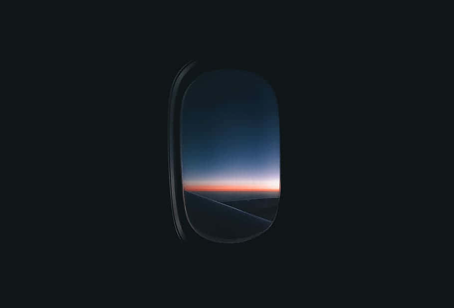 飛機窗顯示暮色天空，橙色地平線和藍色雲層。