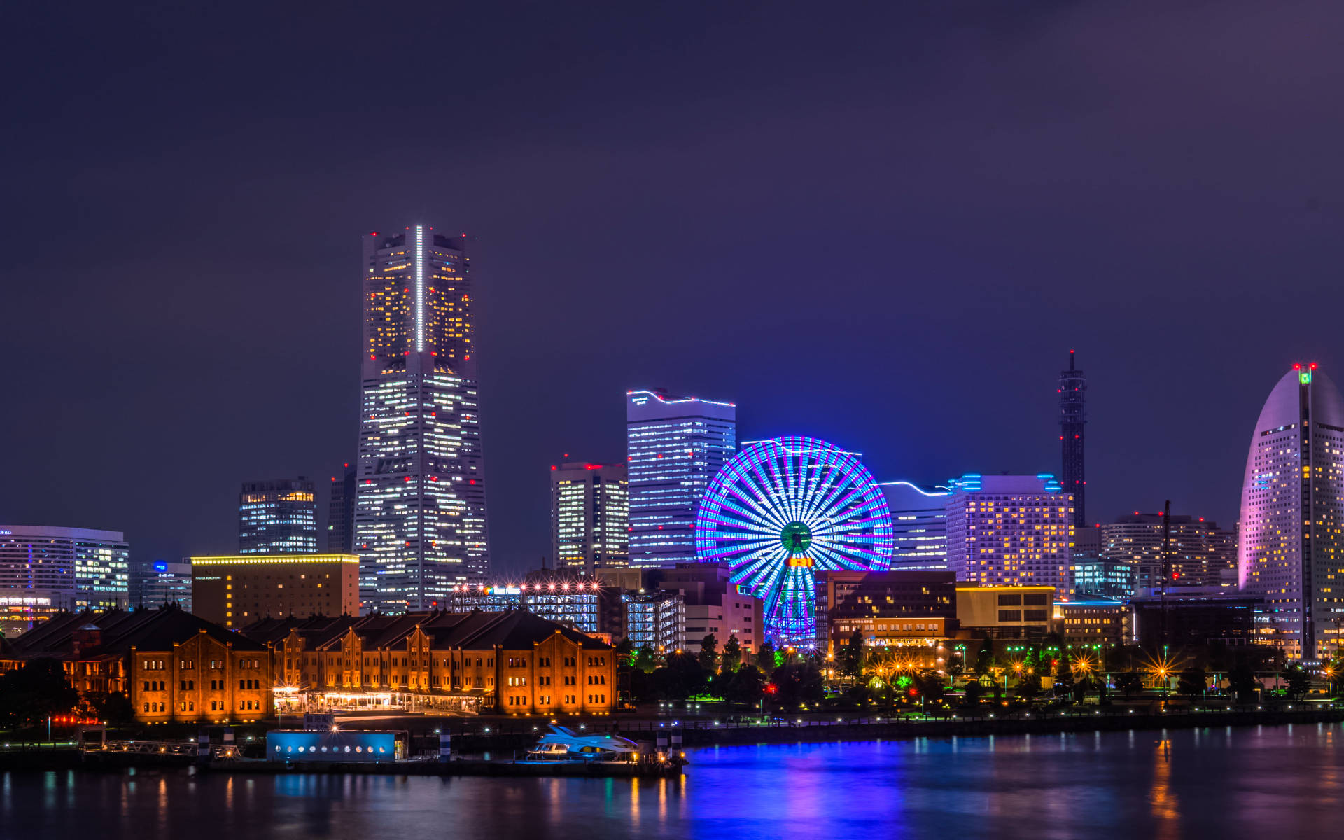 橫濱城市夜景 壁紙 — 充滿活力的夜間城市景觀，閃爍的摩天輪和摩天大樓倒映在平靜的水面上。