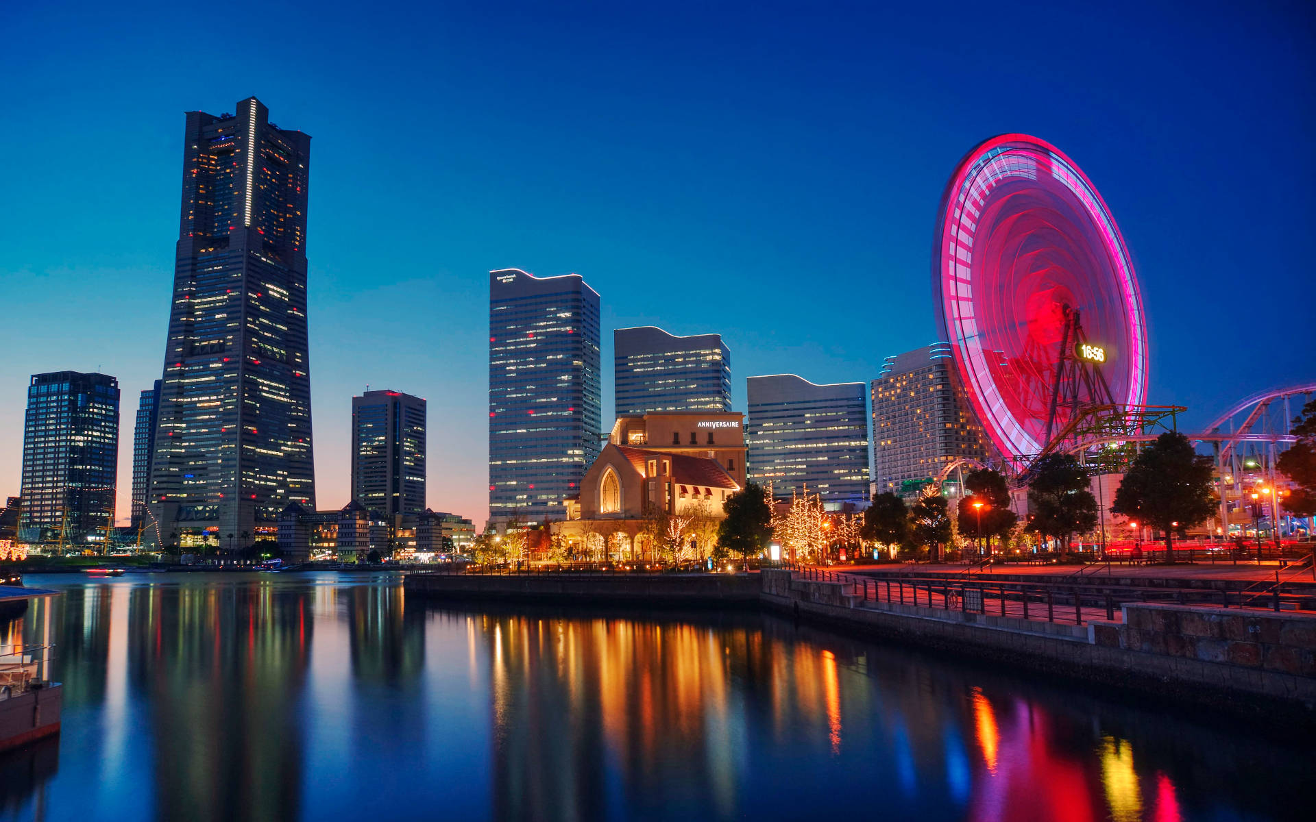 橫濱市夜景 壁紙 — 黃昏時分充滿活力的城市天際線，發光的粉紅色摩天輪倒映在平靜的水面上。
