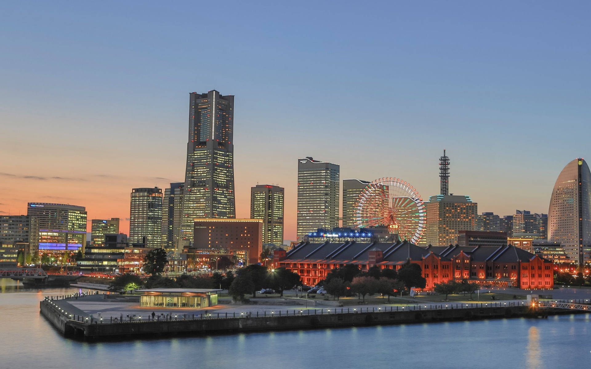 橫濱港口黃金時刻 壁紙 — 橫濱天際線的迷人黃昏景色，閃爍的摩天大樓和色彩繽紛的摩天輪倒映在平靜的水面上。