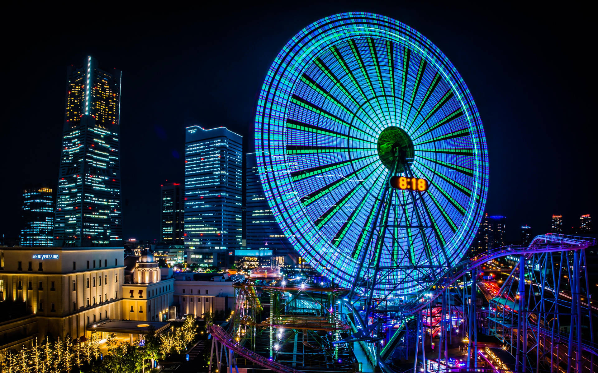 橫濱遊樂園夜景 壁紙 — 一個耀眼的藍色霓虹摩天輪主導了充滿活力的夜間城市景觀，周圍是發光的摩天大樓和過山車。