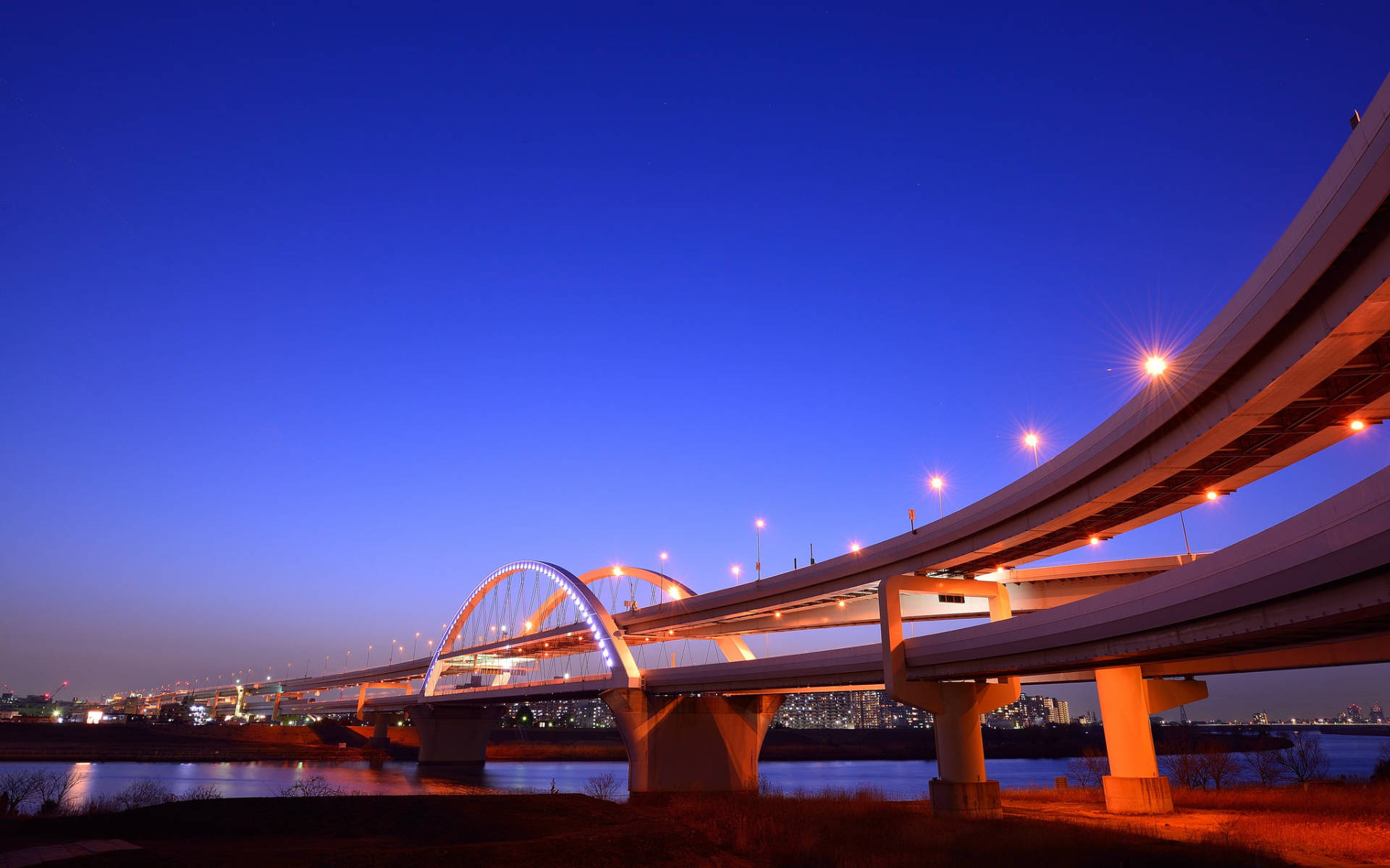 橫濱長橋夜景 壁紙 — 一座現代化的照明橋樑在黃昏時優雅地彎曲在河上，城市燈光倒映在水中。