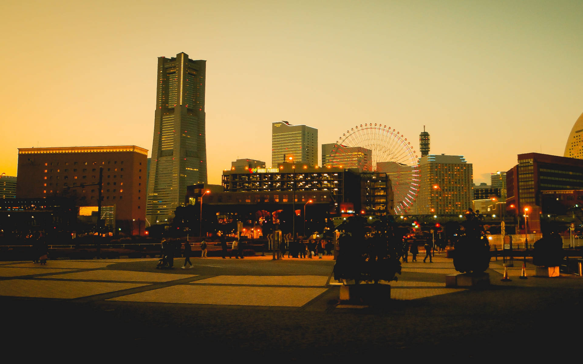 橫濱黃金時刻城市風光 壁紙 — 金色夕陽灑落在繁華的城市廣場上，映襯著人們的剪影和包括摩天輪在內的宏偉建築。