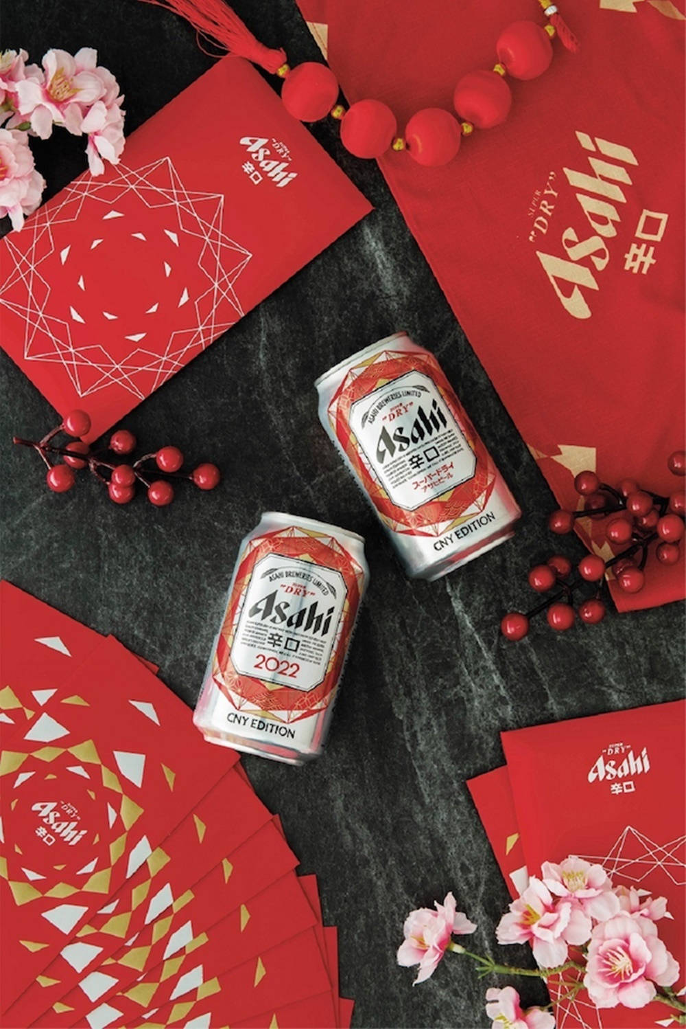 檳城美食與朝日超乾啤酒 壁紙 — 兩罐Asahi啤酒和紅色農曆新年主題包裝，配以櫻花和漿果，置於深色大理石表面上。