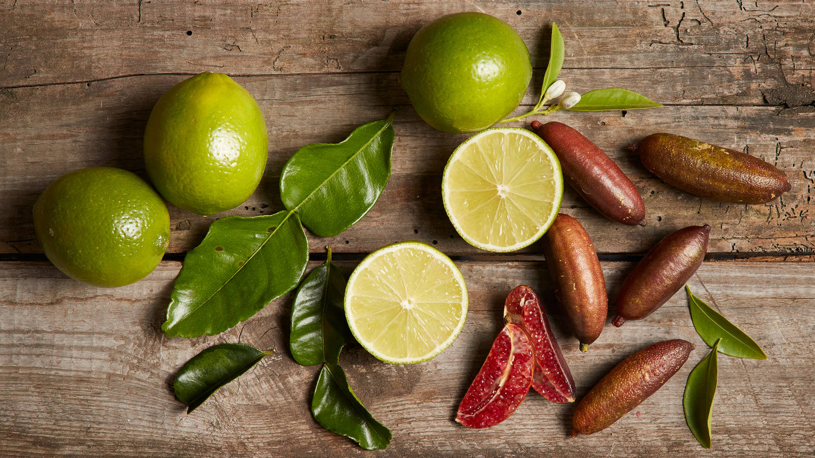 檸檬、青檸與指 lime 壁紙 — 新鮮青檸和金桔連葉子擺放在風化的木質表面上。