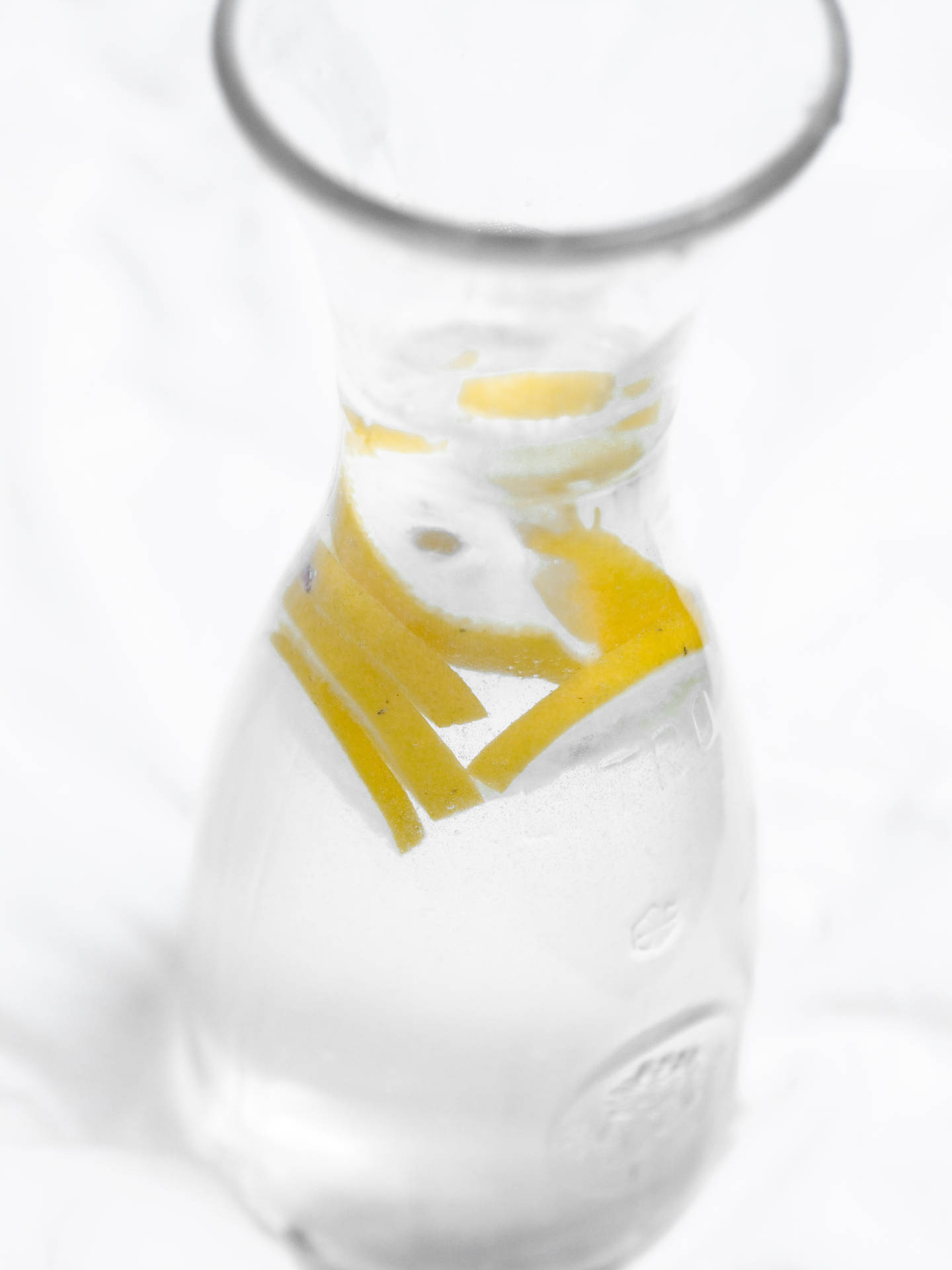 一個玻璃水瓶，水中有檸檬片，放在白色表面上。