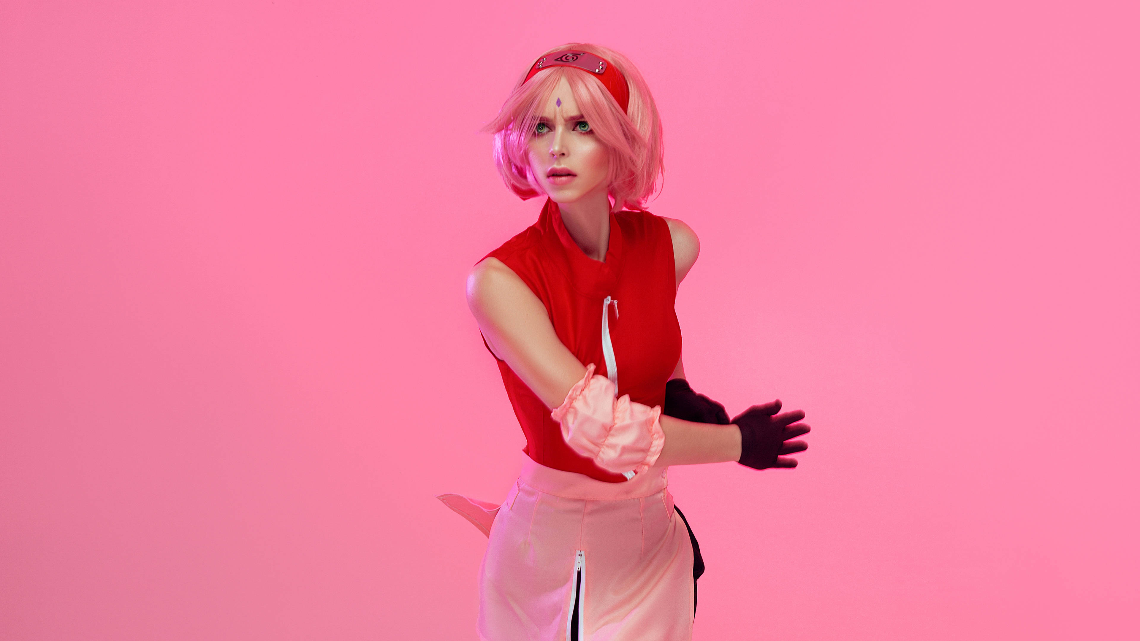 櫻花 HARUNO 外國 Cosplayer 壁紙 — 一位扮演粉紅色頭髮動漫角色的cosplayer在純粉紅色工作室背景前動態擺姿勢。