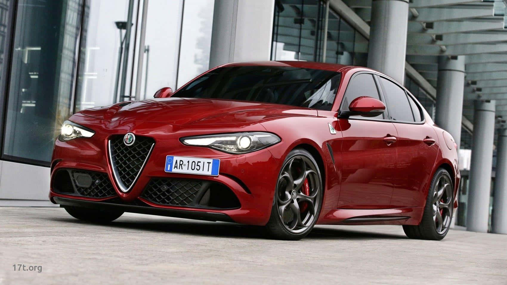 欣賞Alfa Romeo的風采 壁紙 — 一輛光澤的紅色Alfa Romeo房車停在一棟現代玻璃和鋼結構建築前。