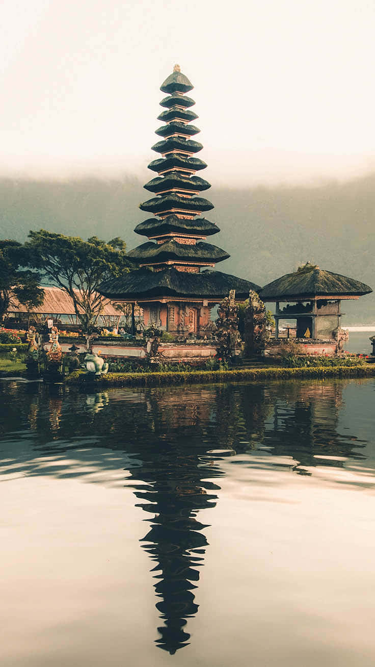 欣賞亞洲自然風光之美 壁紙 — 一座寧靜的峇里島寺廟，層疊的屋頂在平靜的水面上完美倒映，天空柔和迷濛。