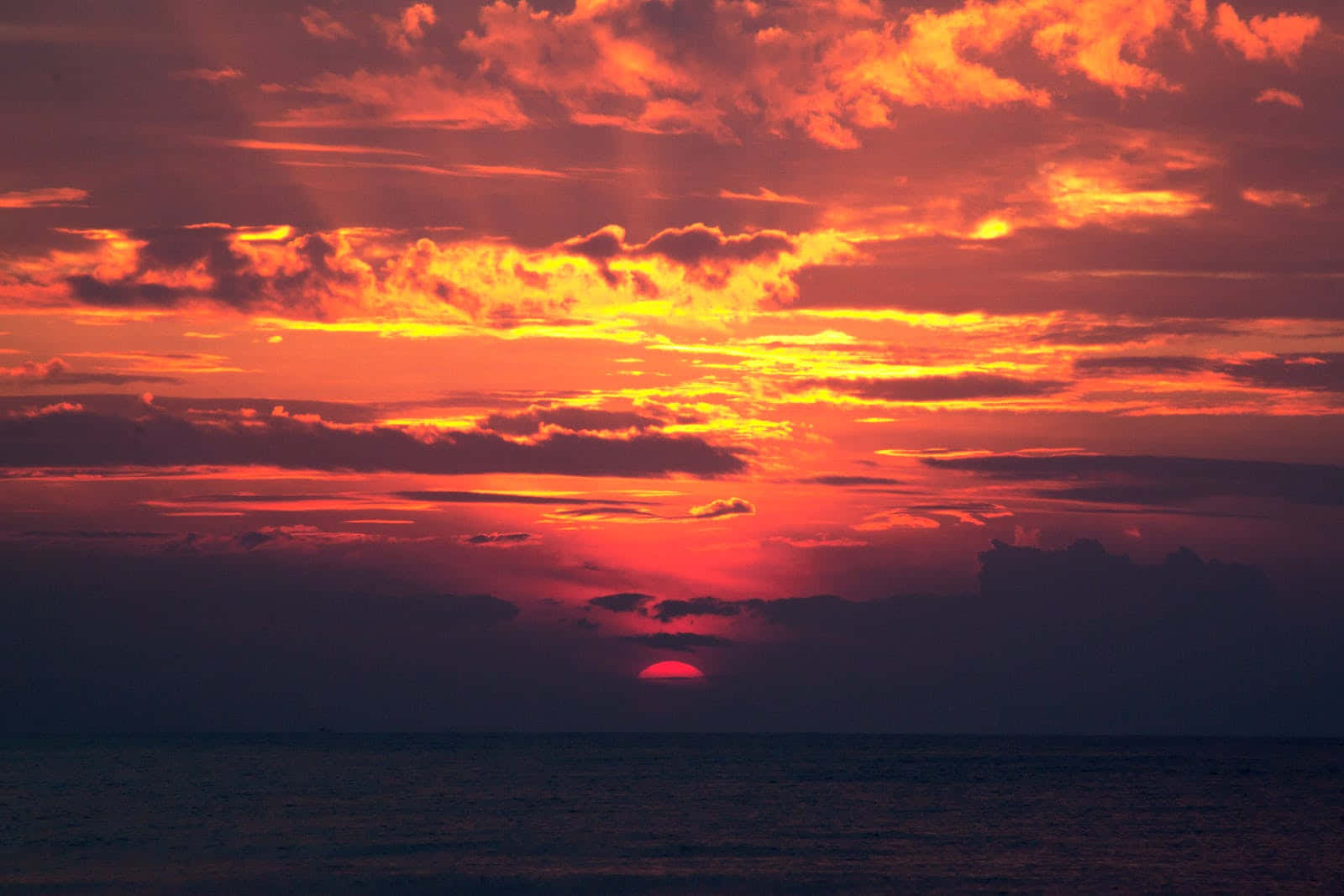 平靜海面上方帶有雲朵的鮮豔橙色和紅色日落。