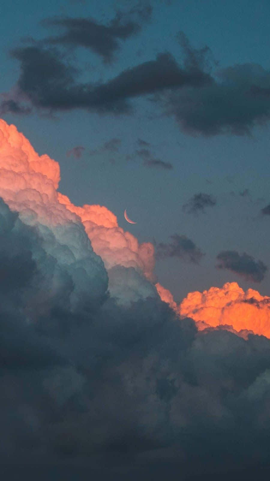 欣賞佈滿美麗雲朵的天空 壁紙 — 一彎新月在火橙色和深暮藍色的戲劇性雲層上柔和地發光。