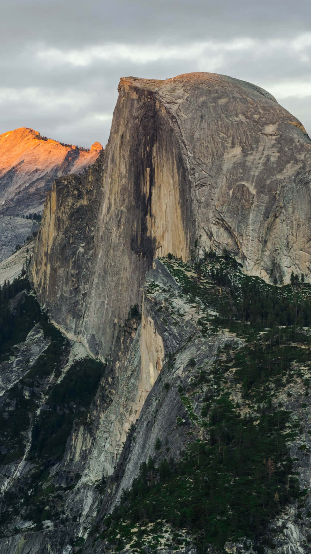 Half Dome 山被金色光芒照亮，下方森林，多雲天空