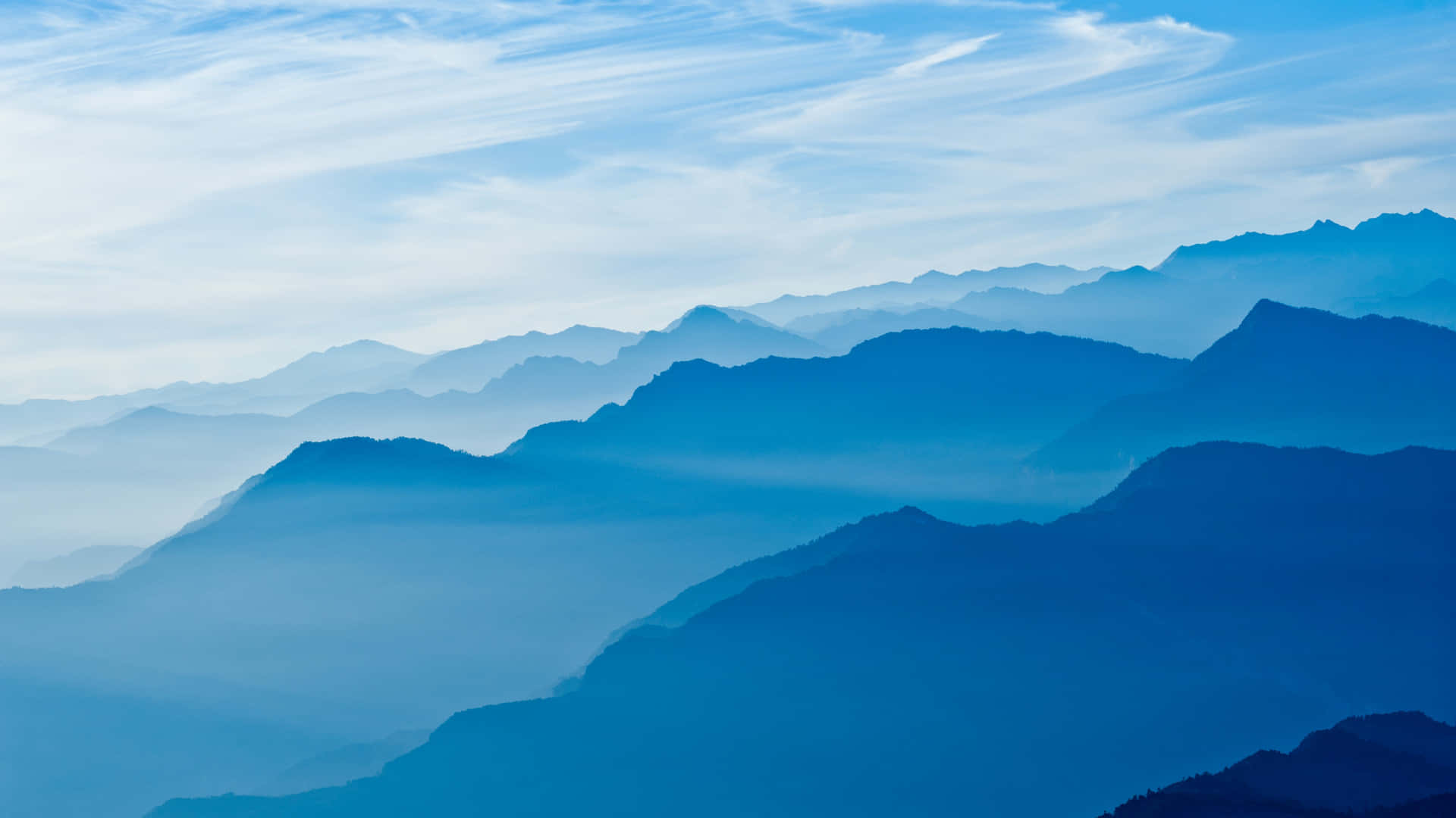 寧靜的山景，層疊的山峰在柔和天空下逐漸融入藍色煙霧中。