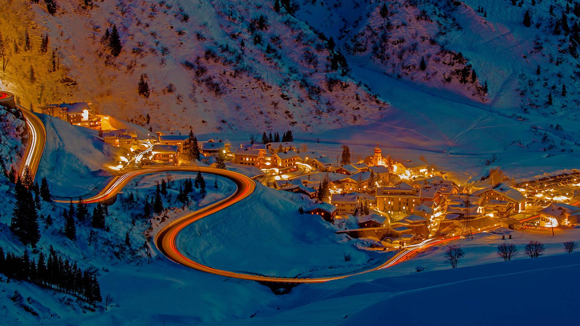 被雪覆蓋的山村被溫暖的燈光照亮，夜晚有發光的道路軌跡。