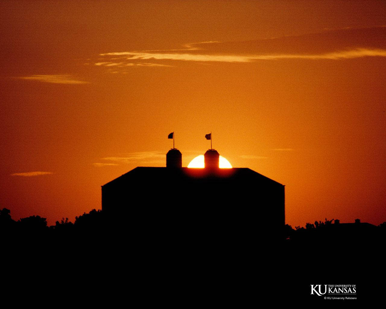 穀倉剪影映襯著鮮豔的橙色夕陽，太陽位於兩個筒倉之間。