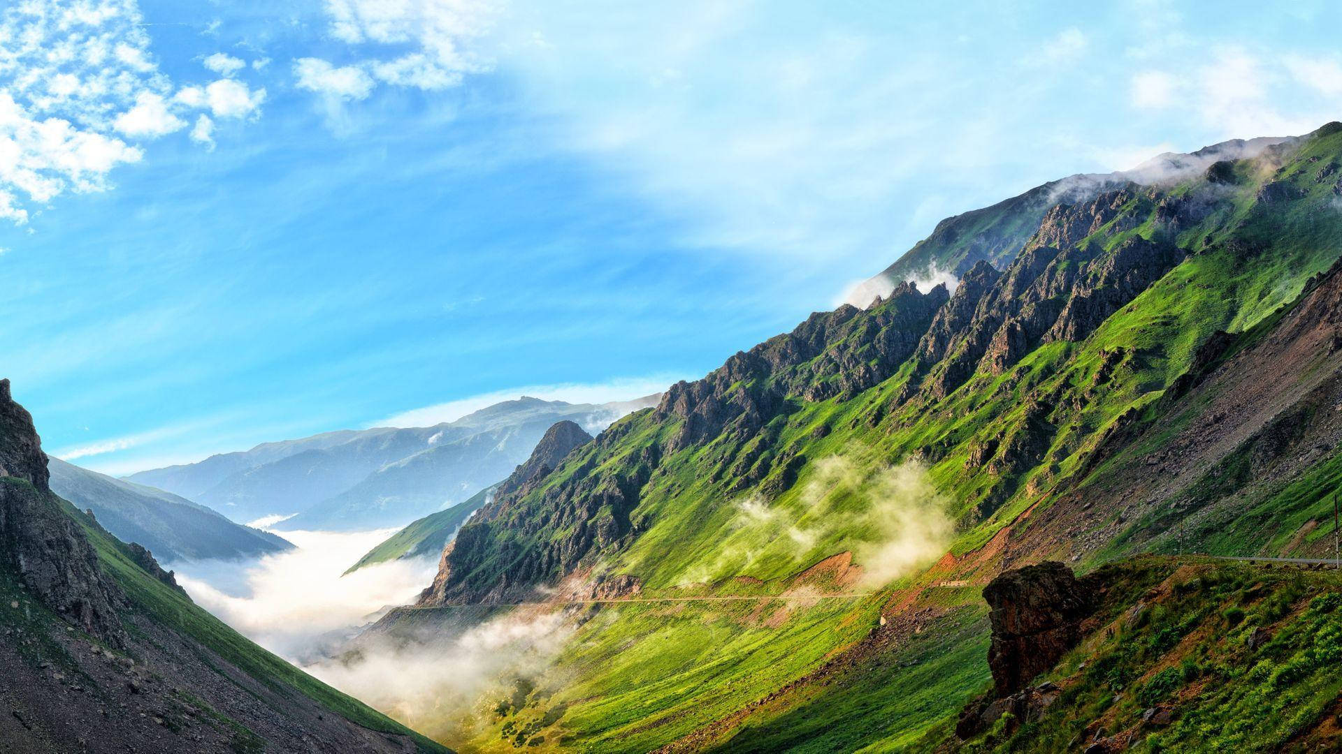 茂密的綠色山脈，山谷中霧雲繚繞，天空清澈湛藍。
